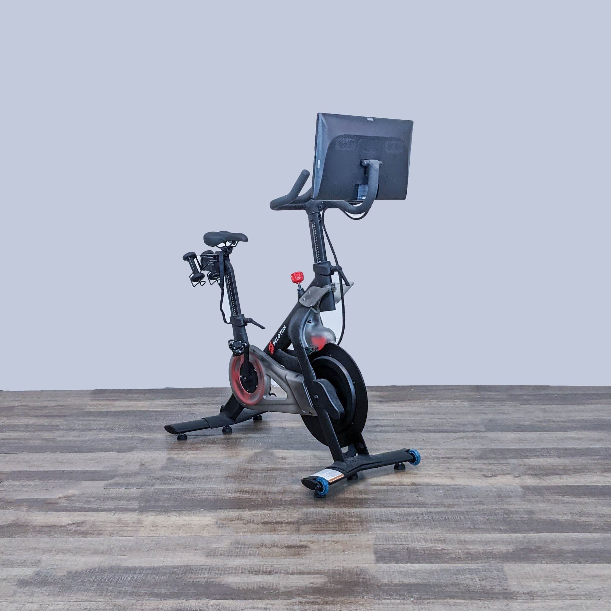 Peloton Indoor Exercise Bike positioned at an angle showing interactive touchscreen and sleek frame. Gym Equipment.