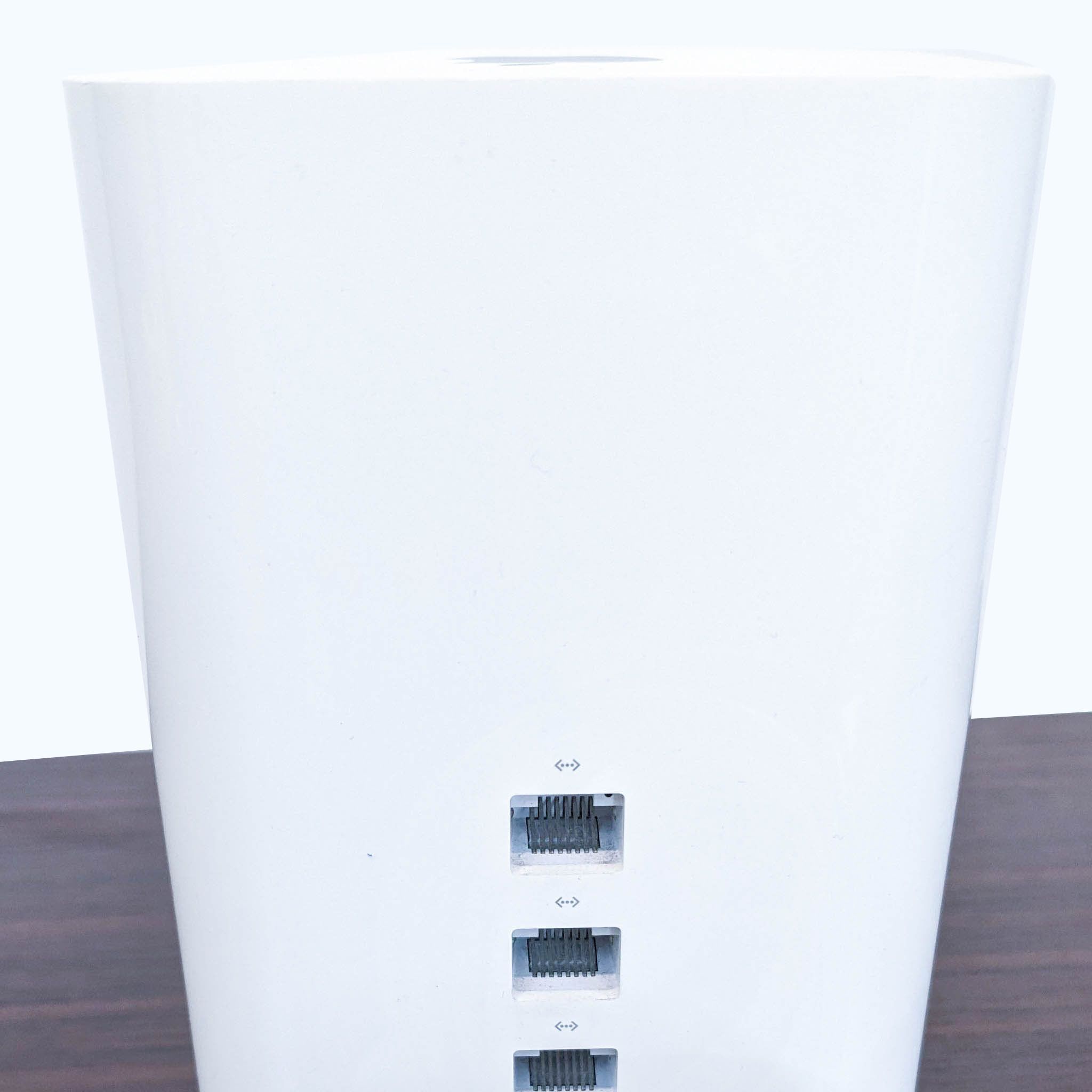 Gently used white cylindrical Apple networking device with multiple ports visible, on a wooden surface.