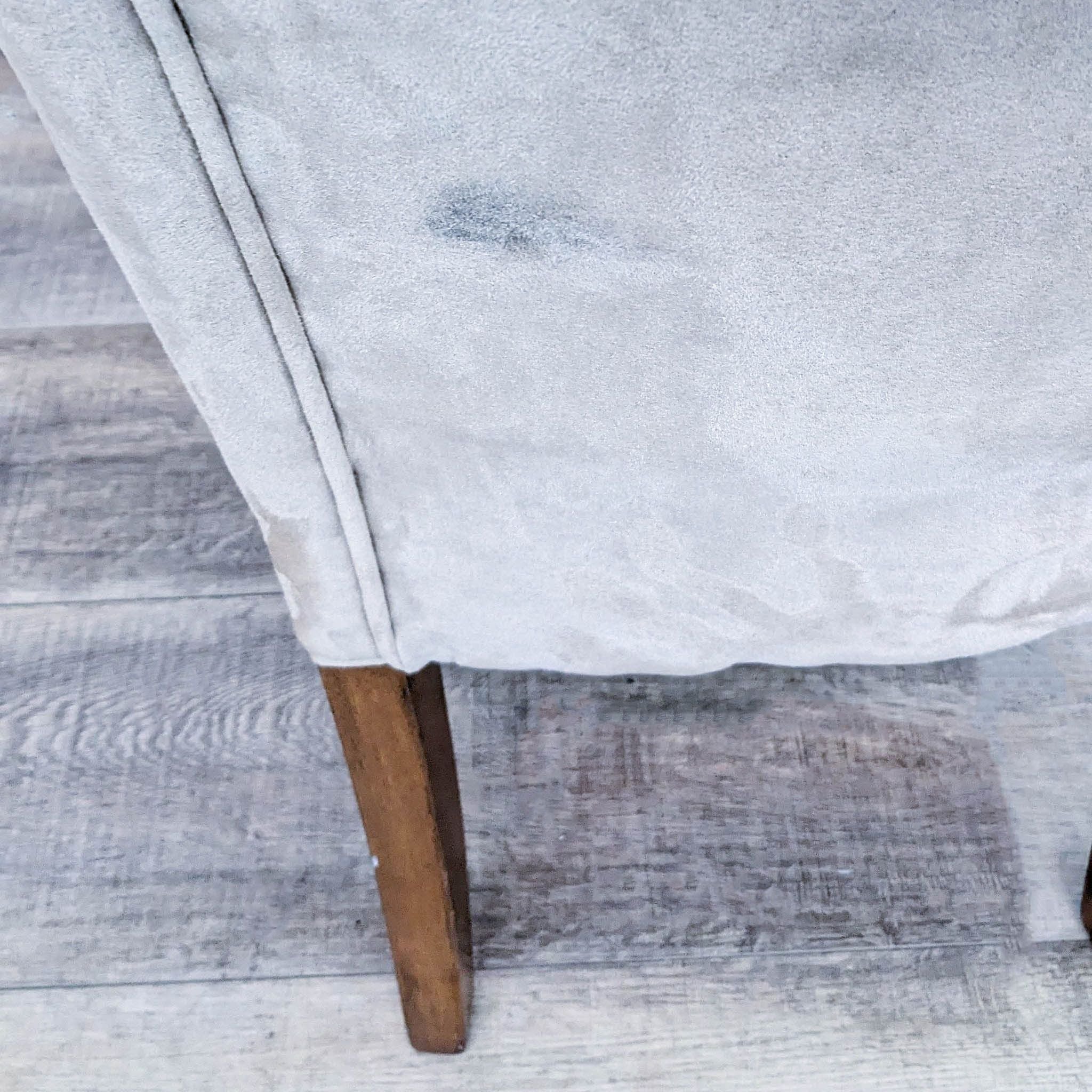 Close-up on the wooden leg and faux suede fabric of a Reperch Parsons dining chair against a wooden flooring backdrop.