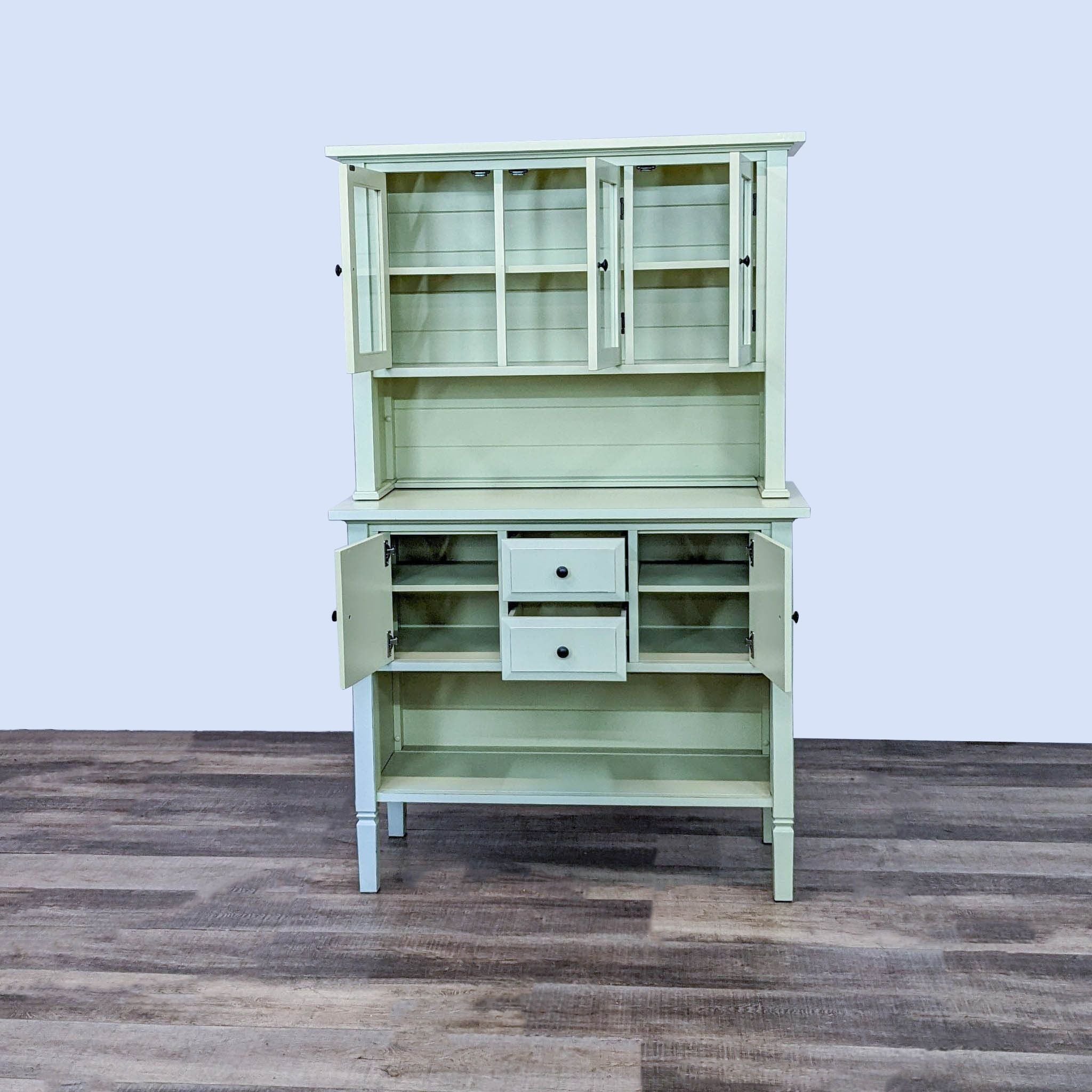 Two-piece Crate & Barrel green hutch with upper glass-front cabinets and lower drawers, designed by Kathleen Wills, showcased on a wooden floor.