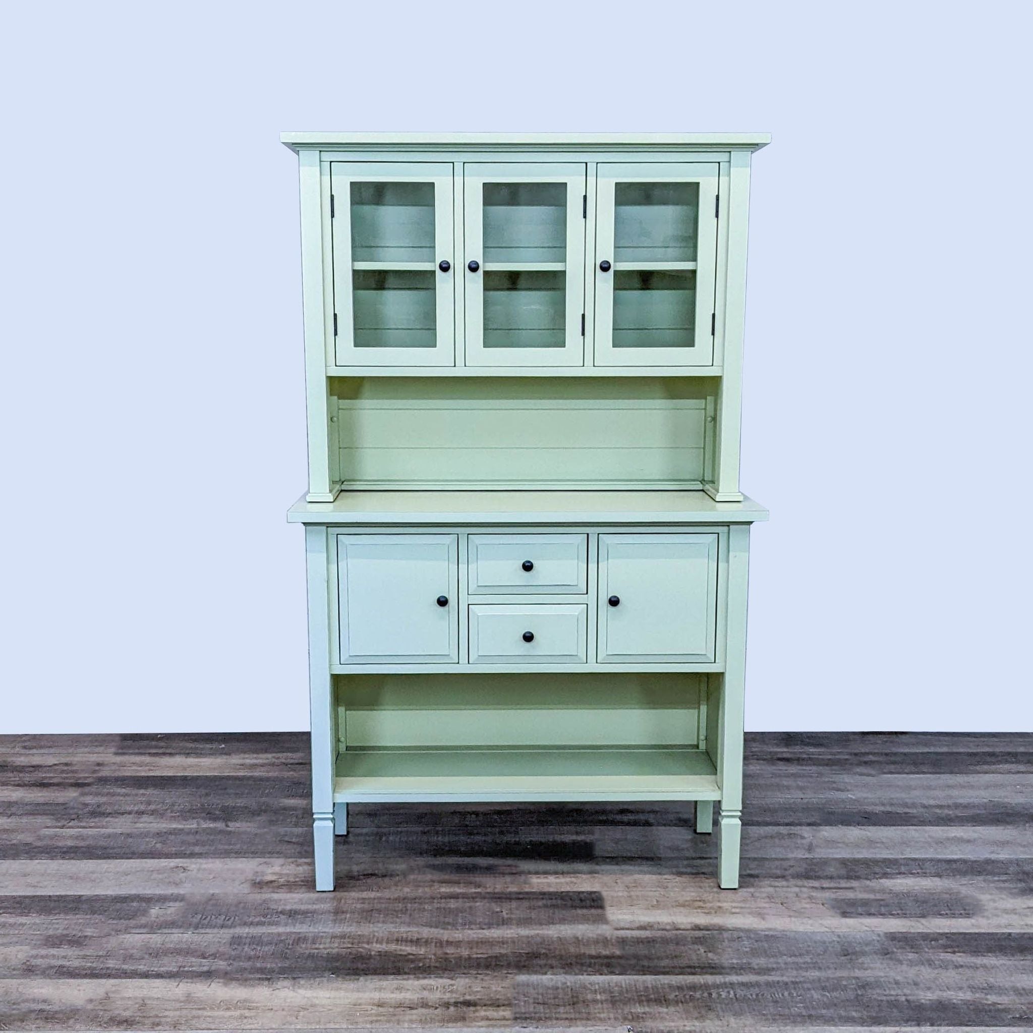 Crate & Barrel farmhouse-style hutch by Kathleen Wills with glass-paneled doors and drawers in a pale green hue, displayed against a white backdrop.