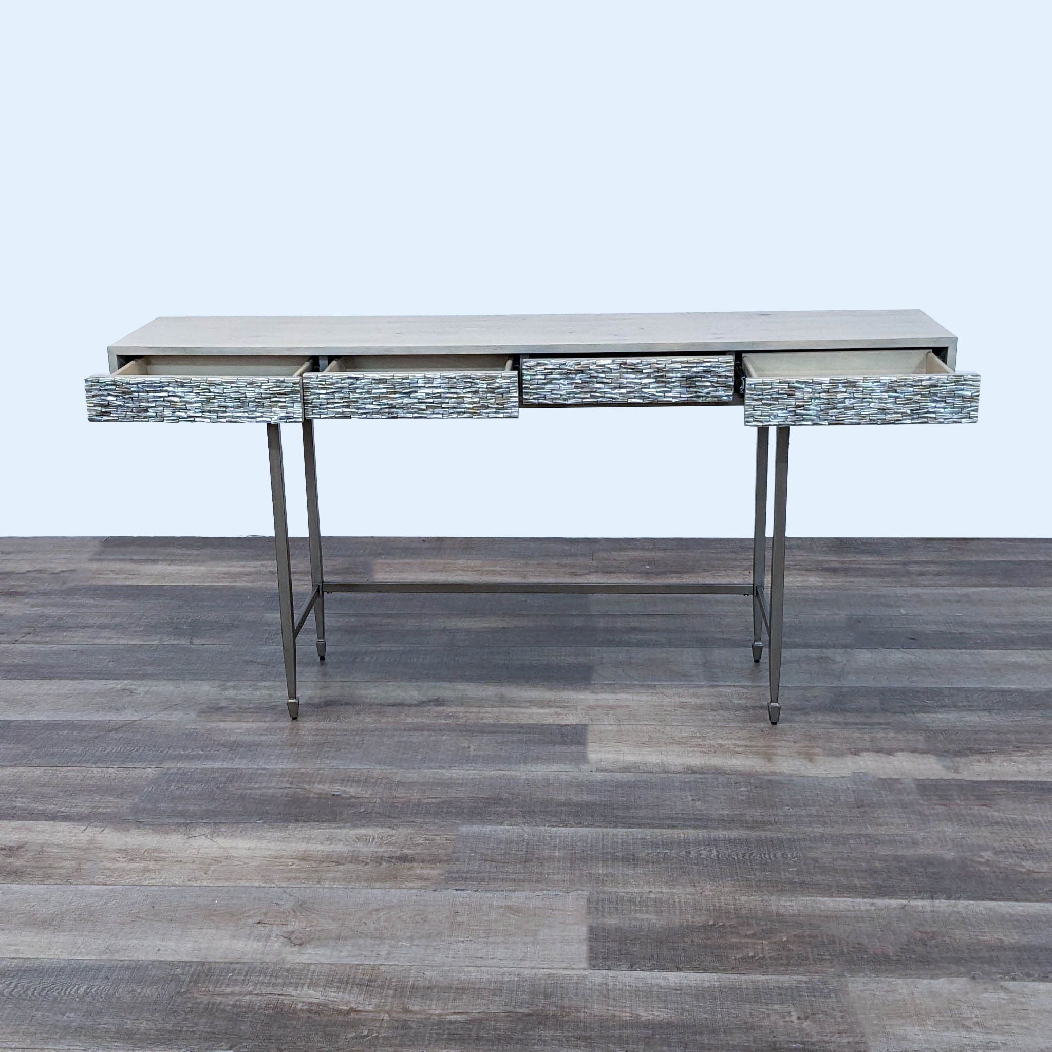 Caracole wood console with open metallic textured drawers revealing storage, on a metal frame against a wooden floor.