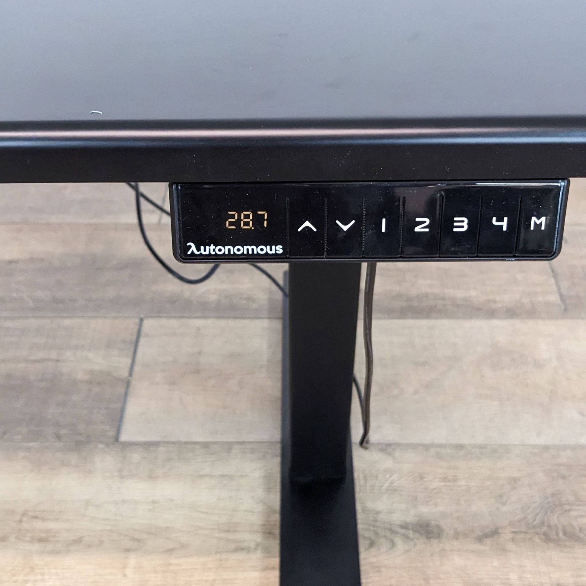 Close-up of Autonomous desk's control panel with height display and black steel legs in background.
