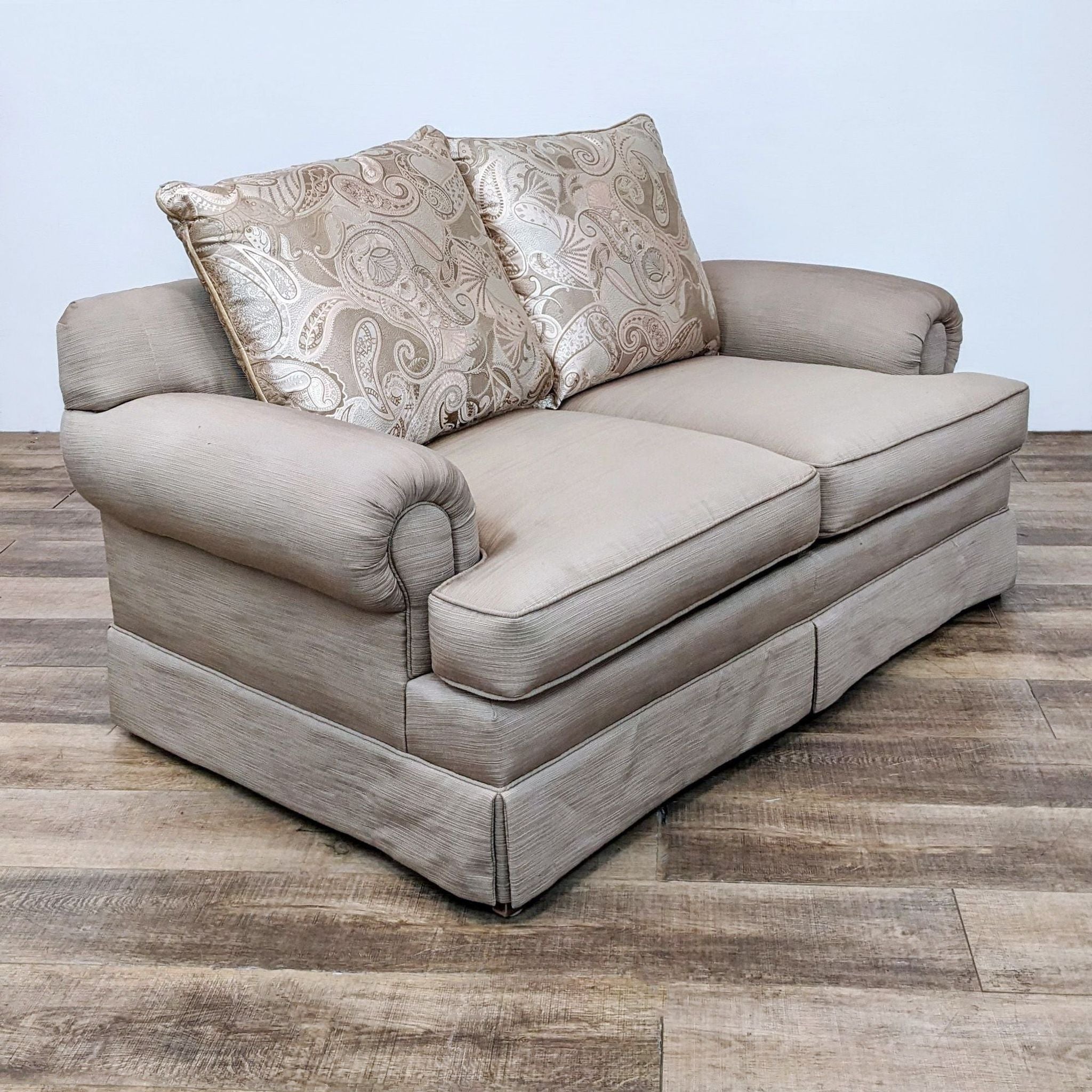 Neutral-tone fabric Loveseat with two back cushions featuring a paisley pattern, set on a wooden floor.