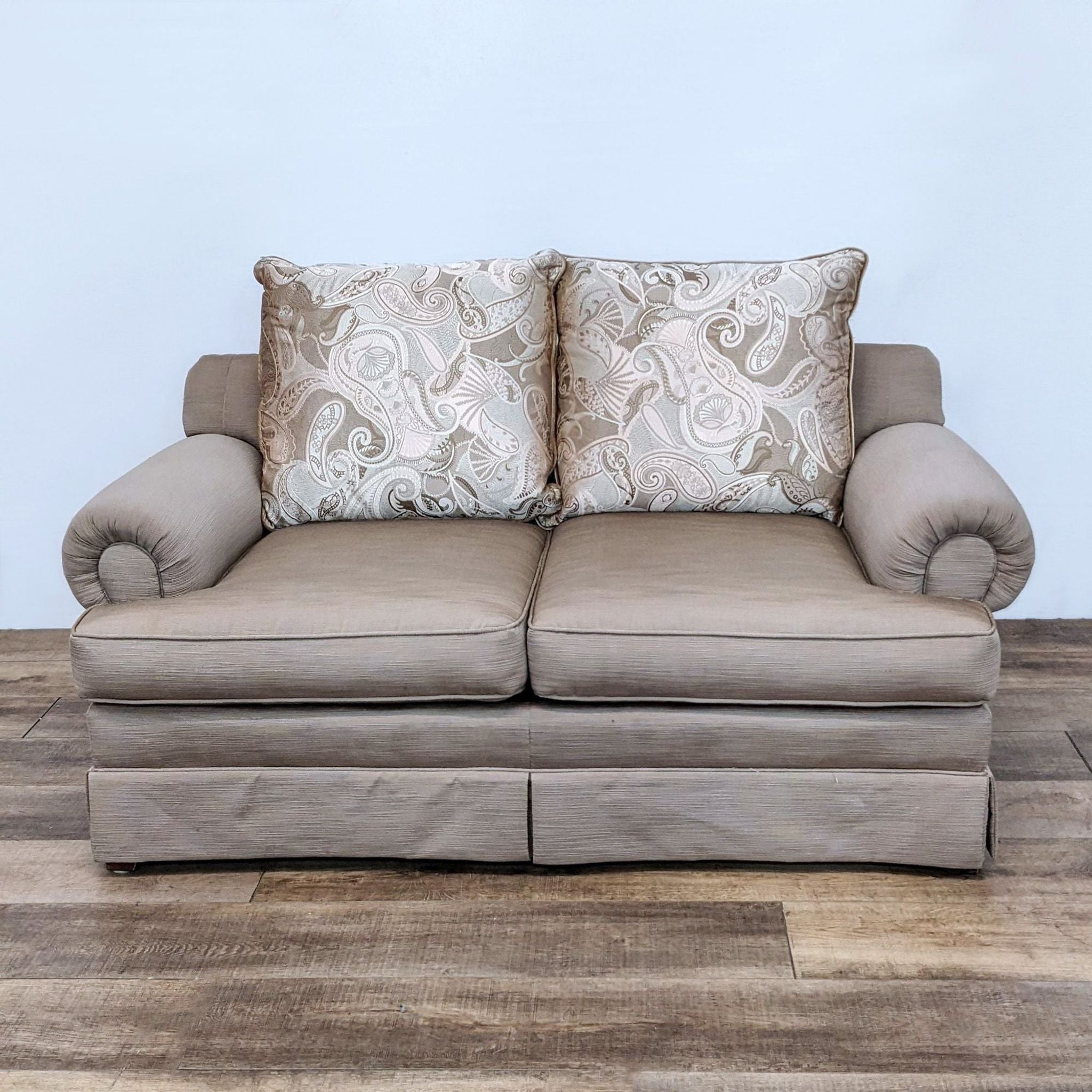 Reperch brand Loveseat in neutral color with roll arms and patterned cushions on a herringbone wood flooring.