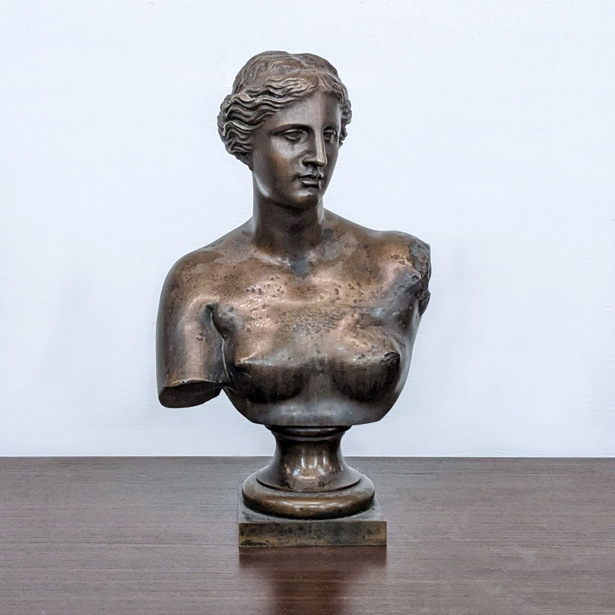 Bronze bust of Venus by Reperch, showing detailed features and upper torso, displayed on a wooden table.
