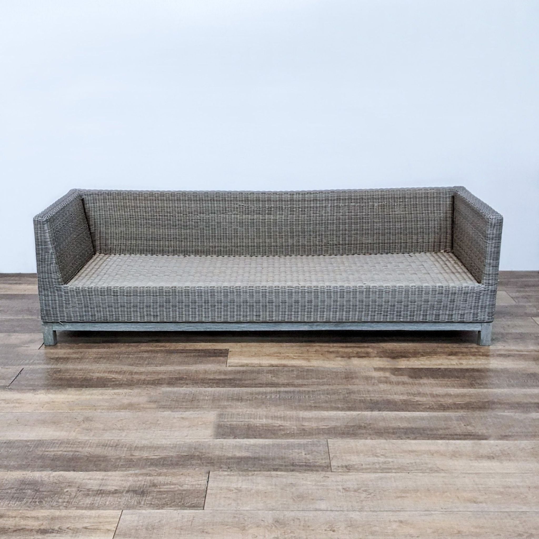 Resin wicker outdoor sofa by Restoration Hardware with a modern teak wood frame on hardwood flooring.
