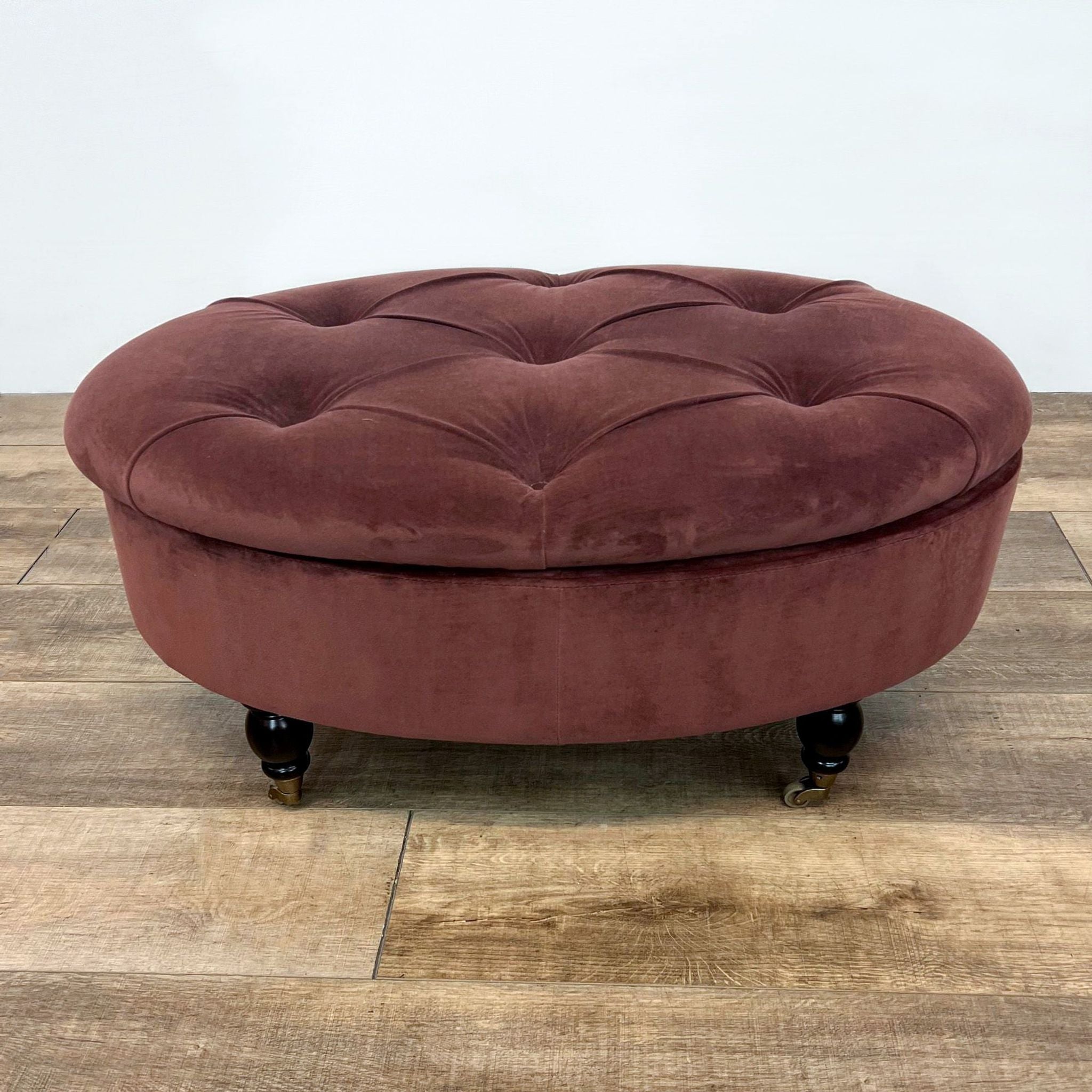 Oval burgundy velvet tufted ottoman with wooden feet and casters, by World Market.