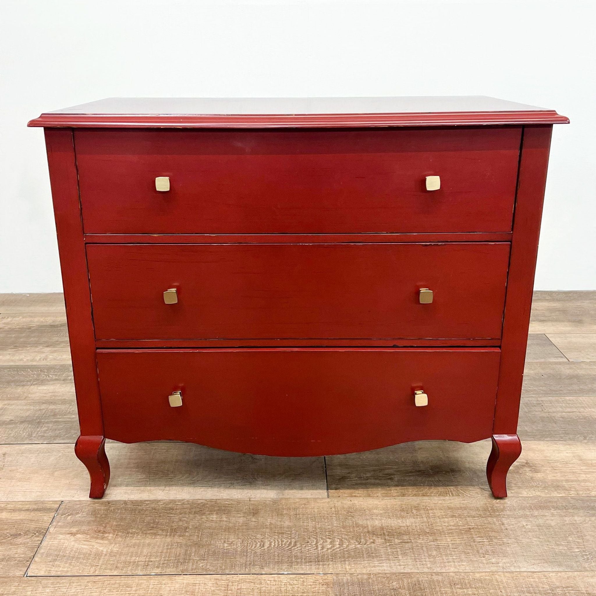Pottery Barn red Luca 3-drawer dresser on a wooden floor, closed drawers with brass knobs.