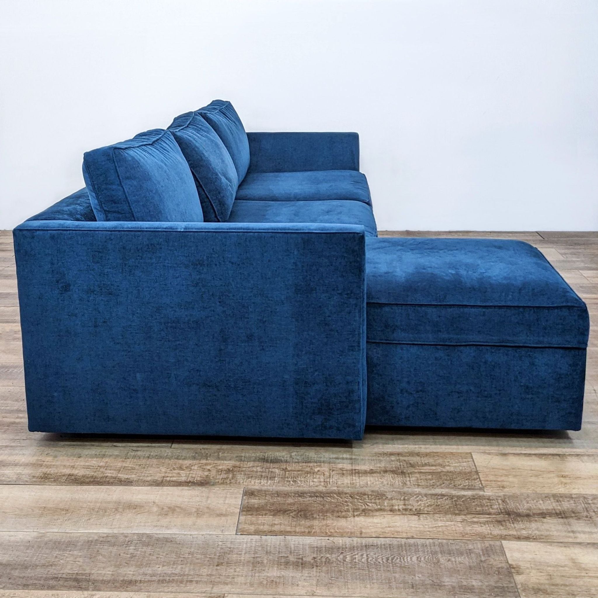 Alt text: Ink blue West Elm distressed velvet two-piece sectional with chaise, narrow arms, and clean lines on a wooden floor.