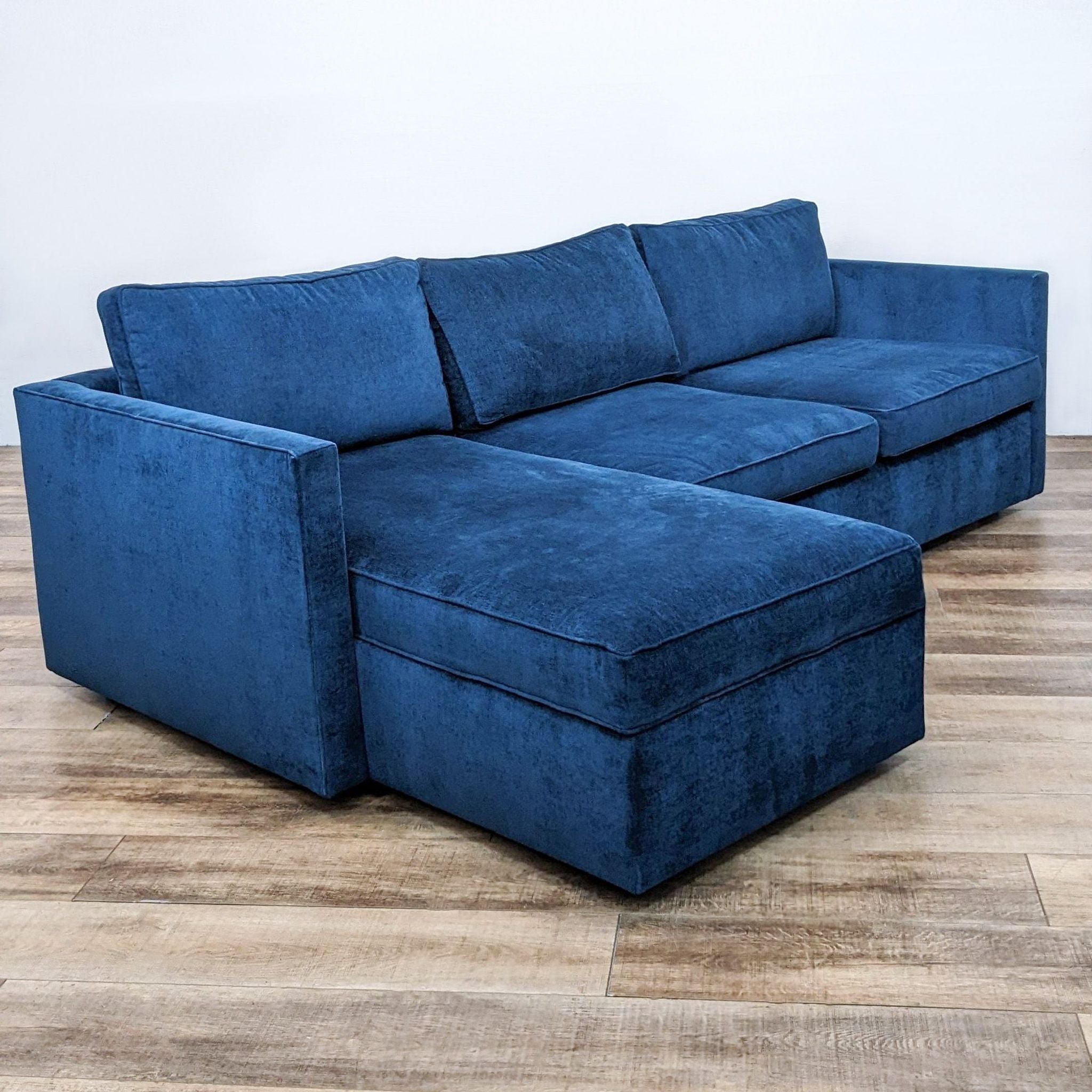 Alt text 2: West Elm sectional in distressed ink blue velvet, showcasing a chaise lounge and streamlined design with modest armrests, presented on a plank-style floor.