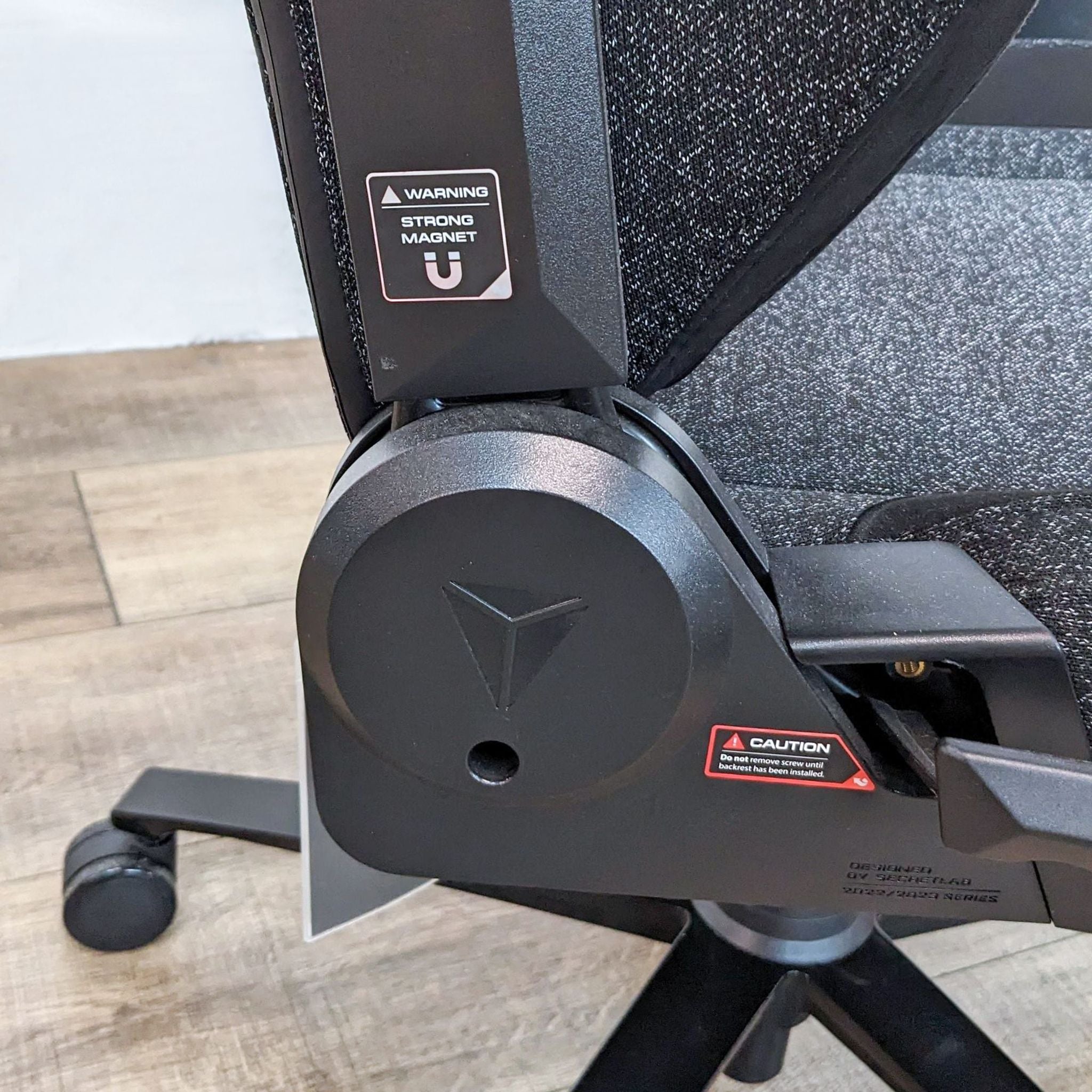 Close-up of the Secretlab Titan Evo gaming chair's hydraulic recline mechanism with warning labels.