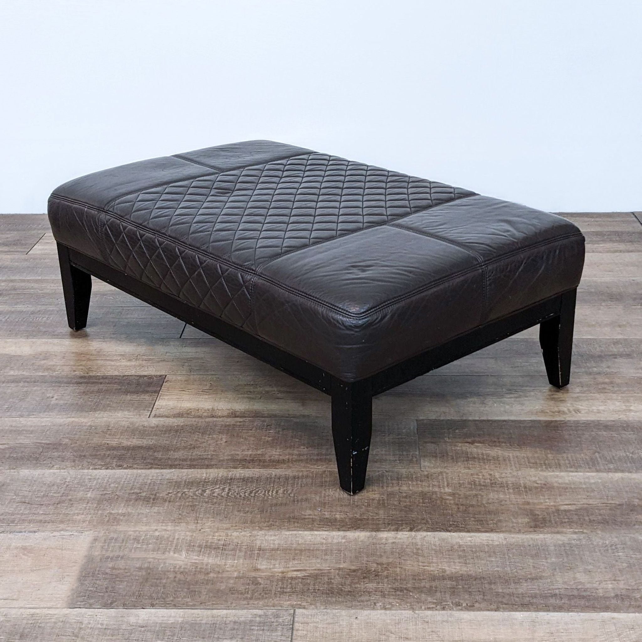 Alt text 2: Frontal view of a brown leather Reperch ottoman with diamond stitching and sturdy wooden feet.