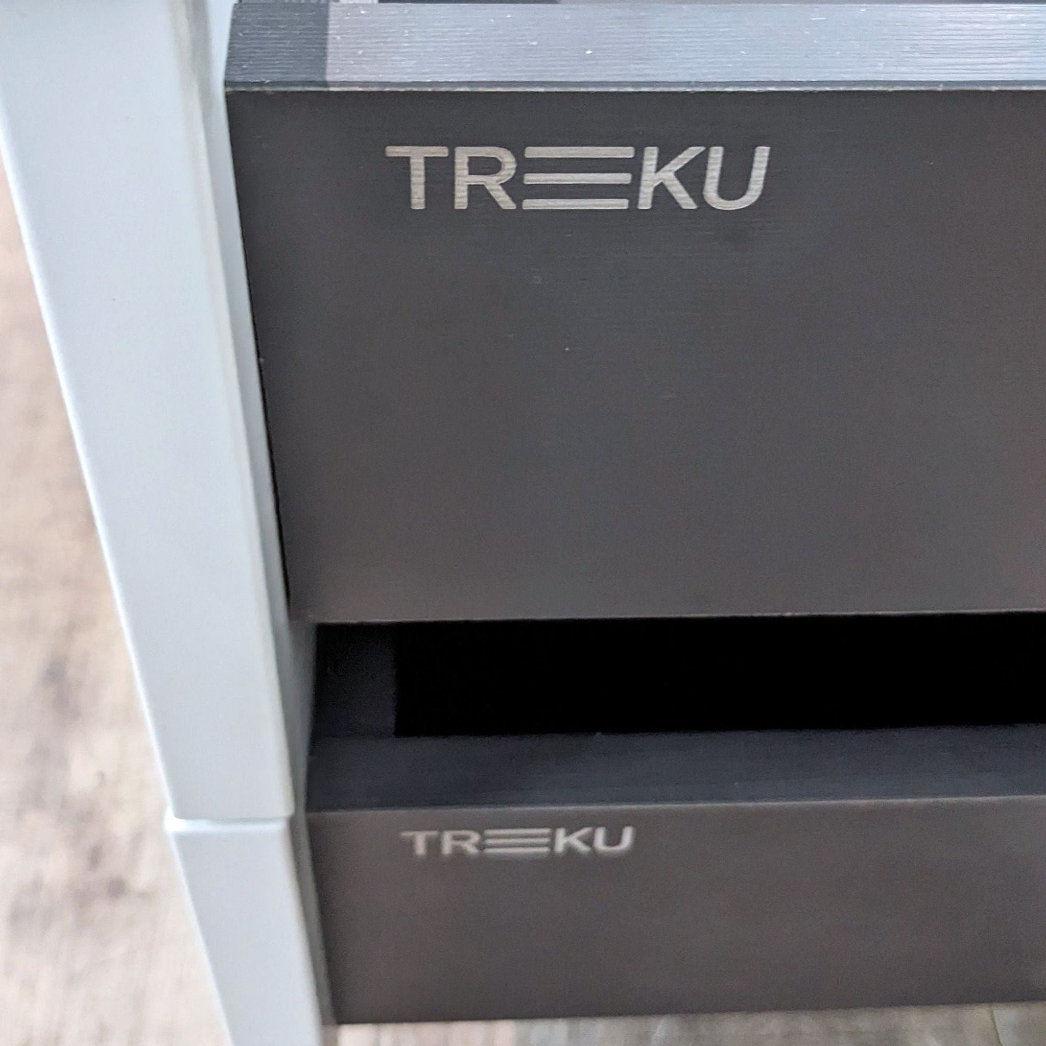 Close-up of Treku brand logo on the two-tone Aura Media Unit by Angel Marti and Enrique Delamo, highlighting the contrast between lacquer and wood veneer.
