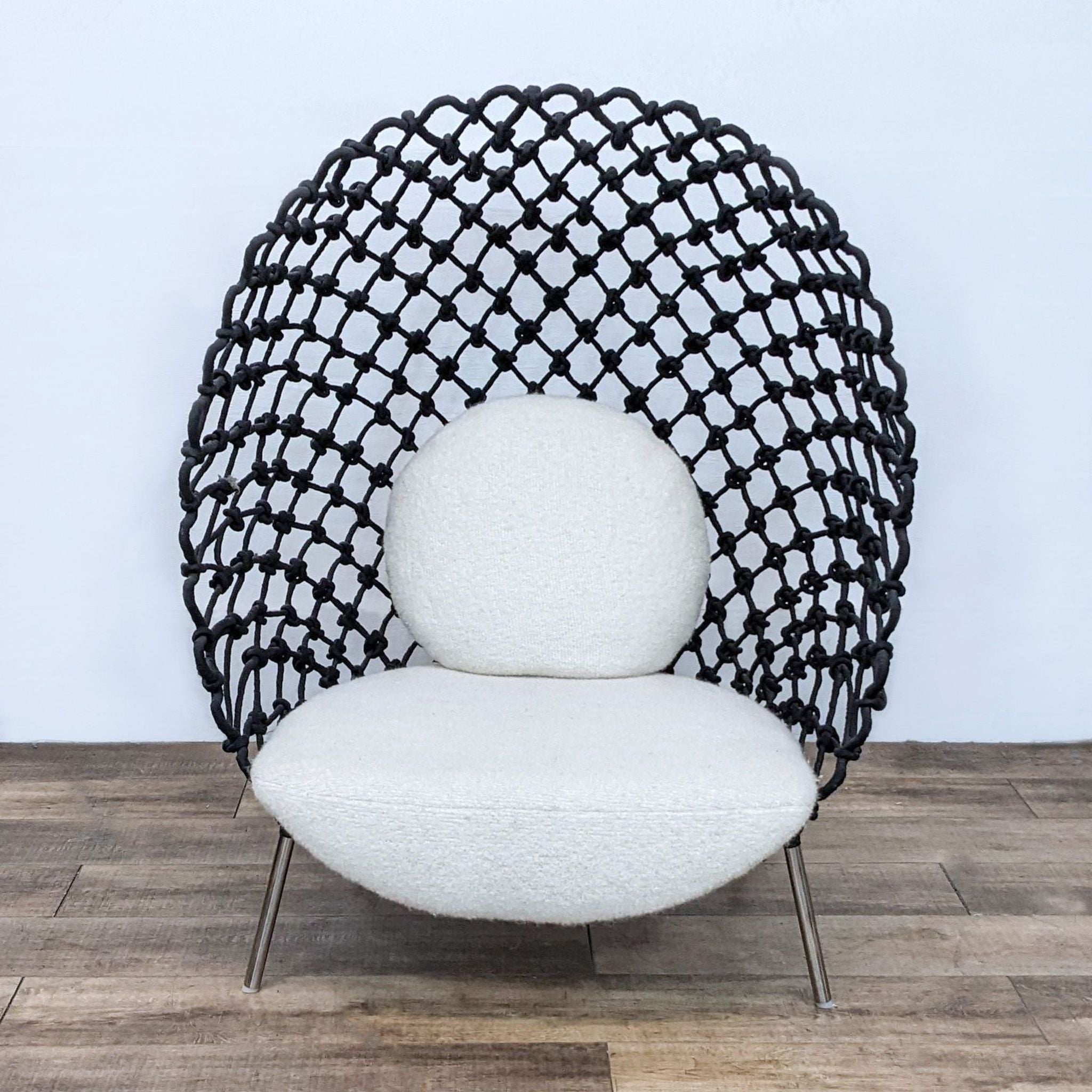 A Reperch Dragnet Lounge Chair with acrylic fabric resembling a fishnet wrapped around a steel frame, set against a plain backdrop.