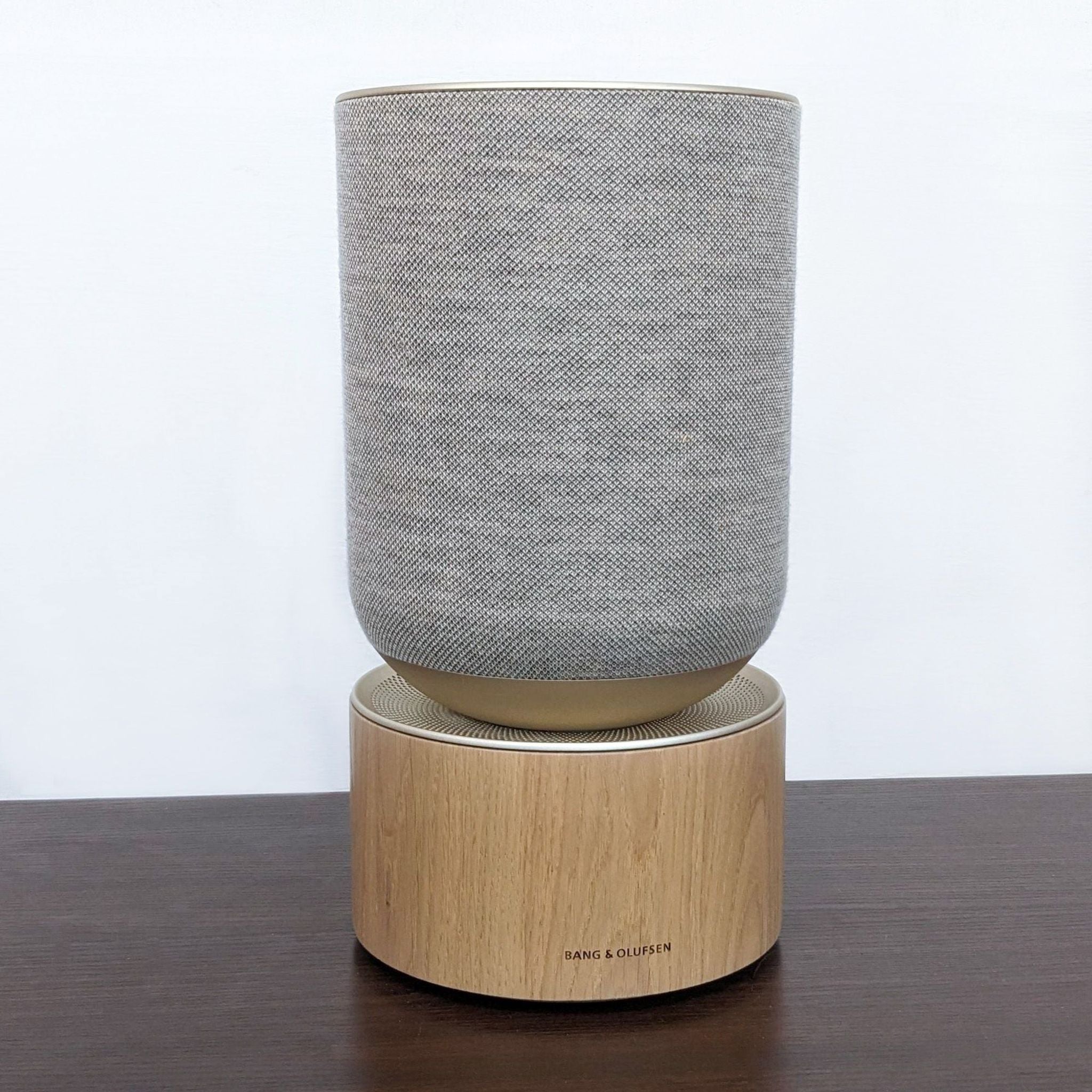 Bang & Olufsen portable speaker in gray on wooden base, against a white background.