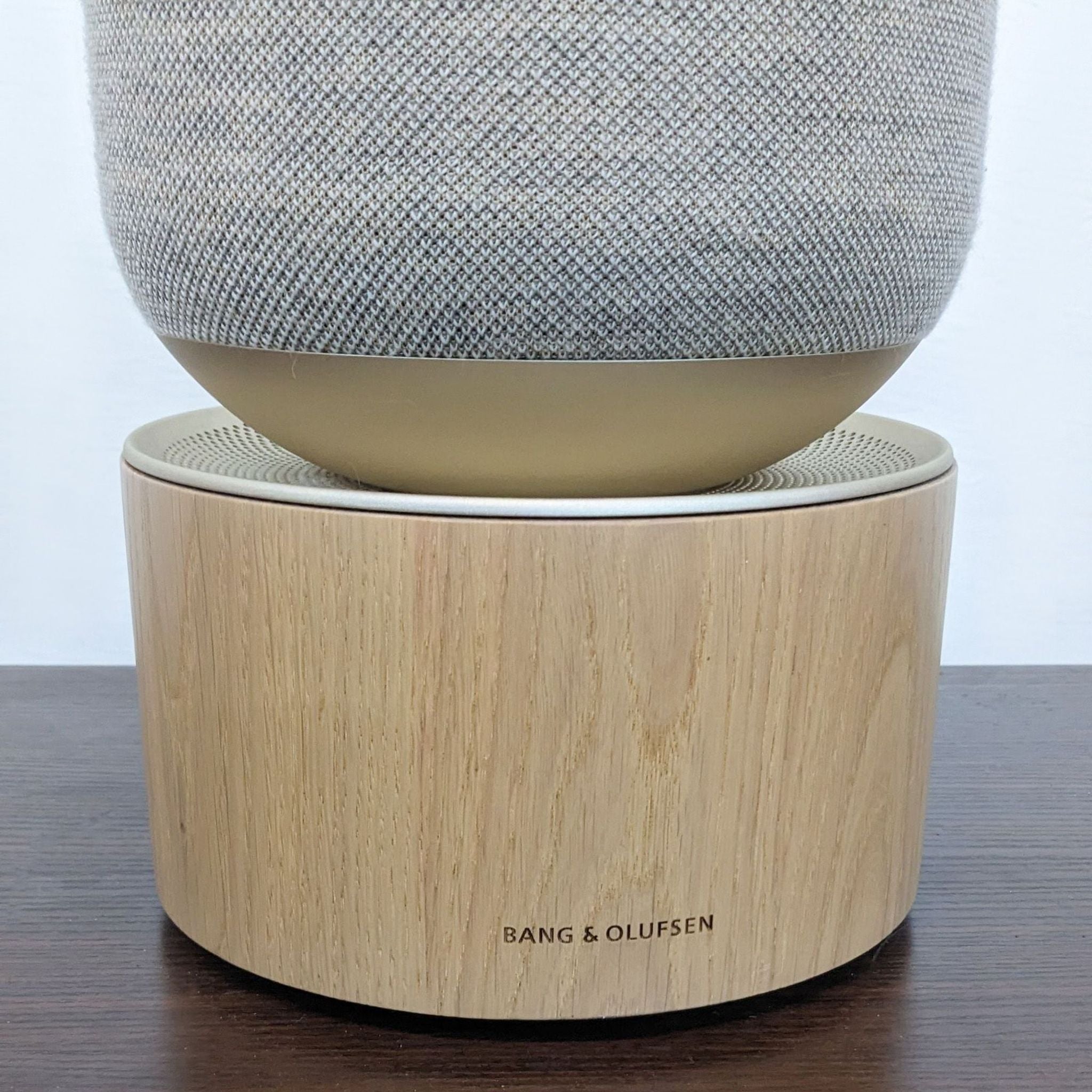 Close-up of Bang & Olufsen speaker's wooden base with brand logo, on dark table.