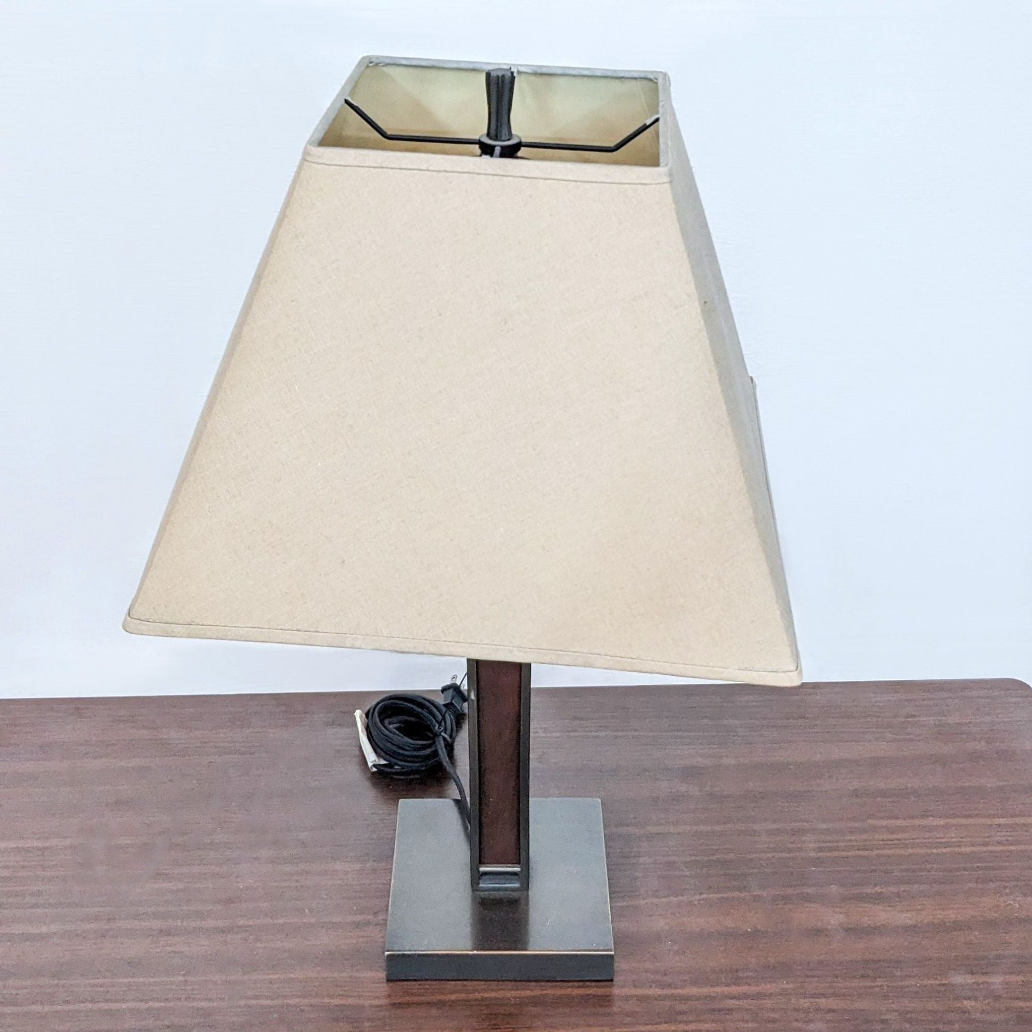 2. Angled view of a Crate & Barrel table lamp showing the beige shade and dark frame on a wood table.