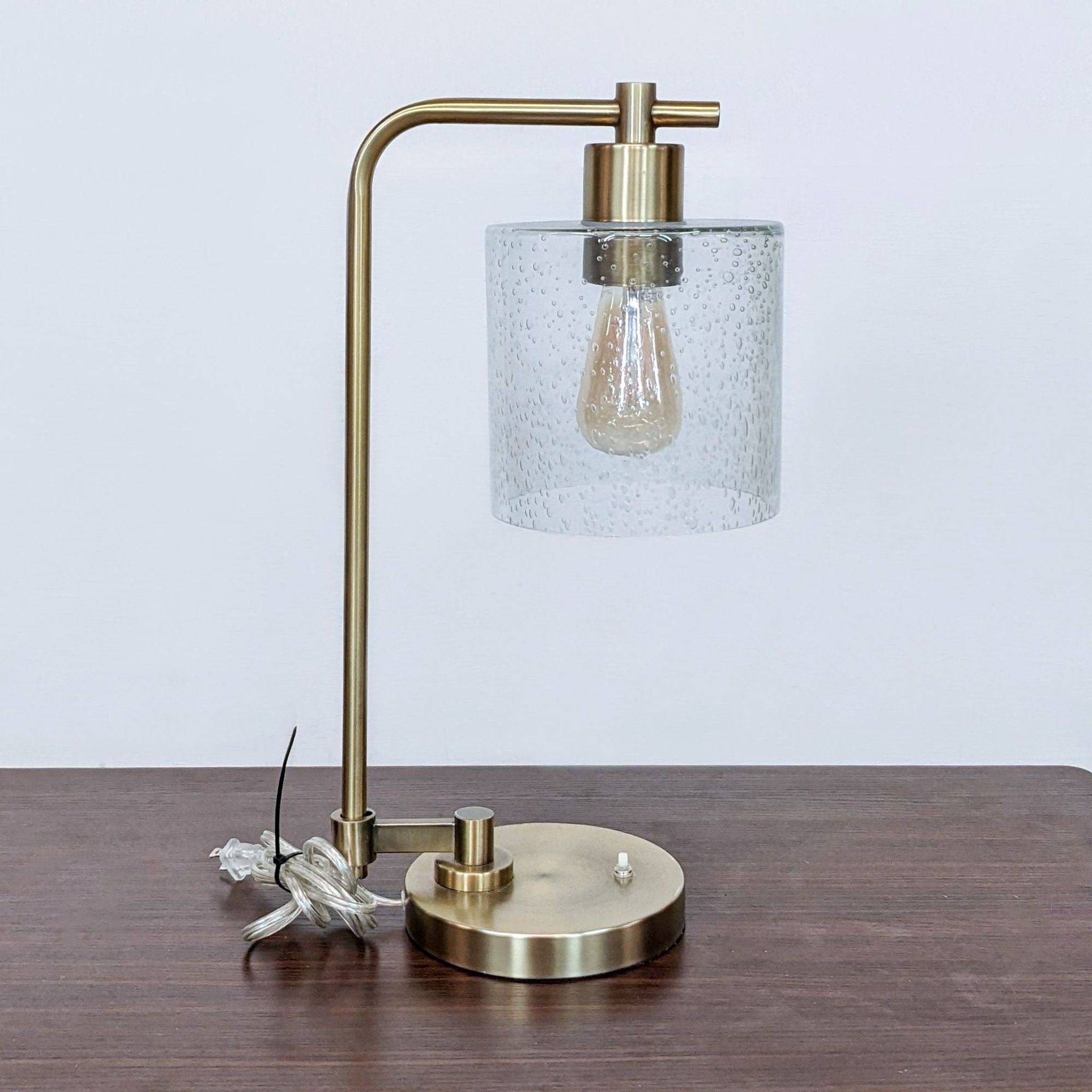 Reperch brand table lamp with a golden base and a clear glass shade with raindrop design on a wooden surface.