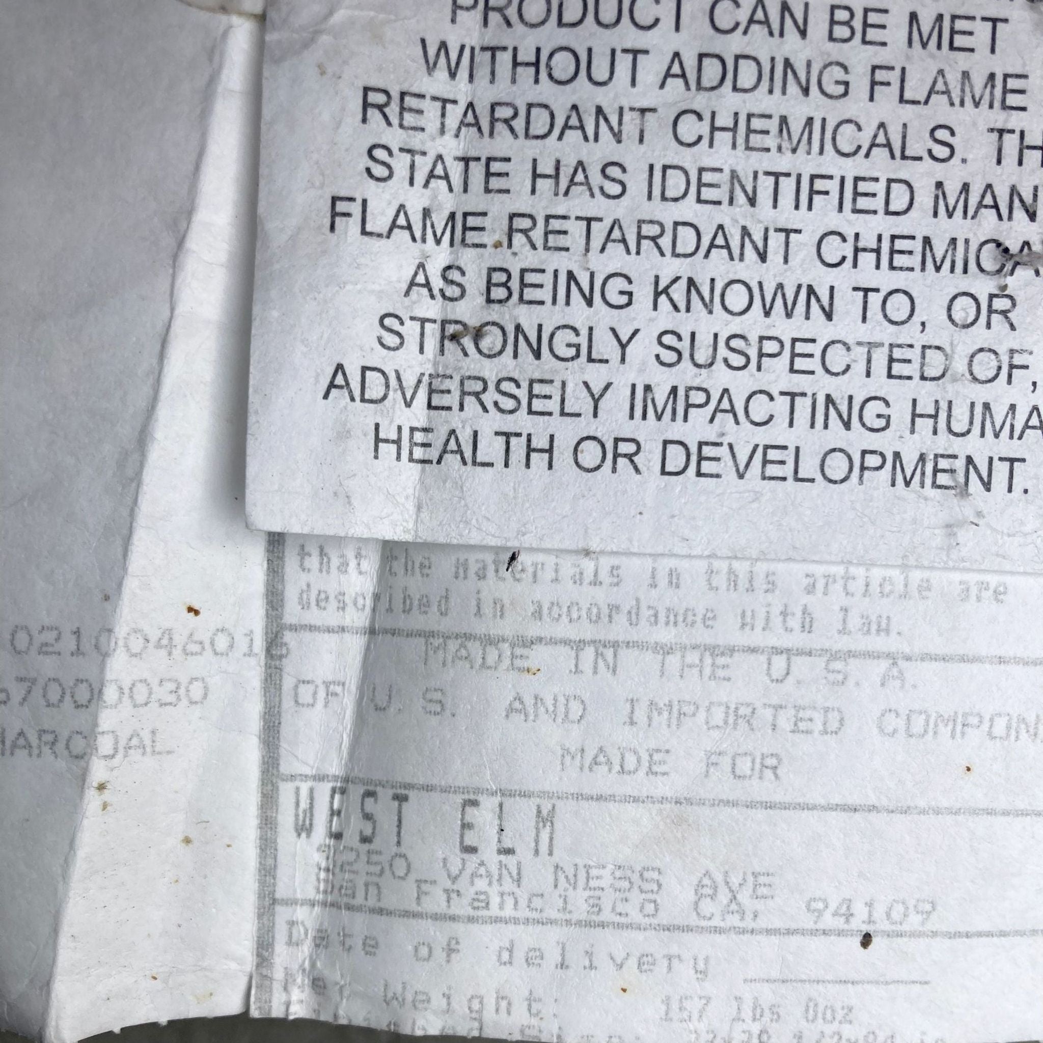 Torn and wrinkled label with text discussing flame retardant chemicals, indicating the item is from West Elm.