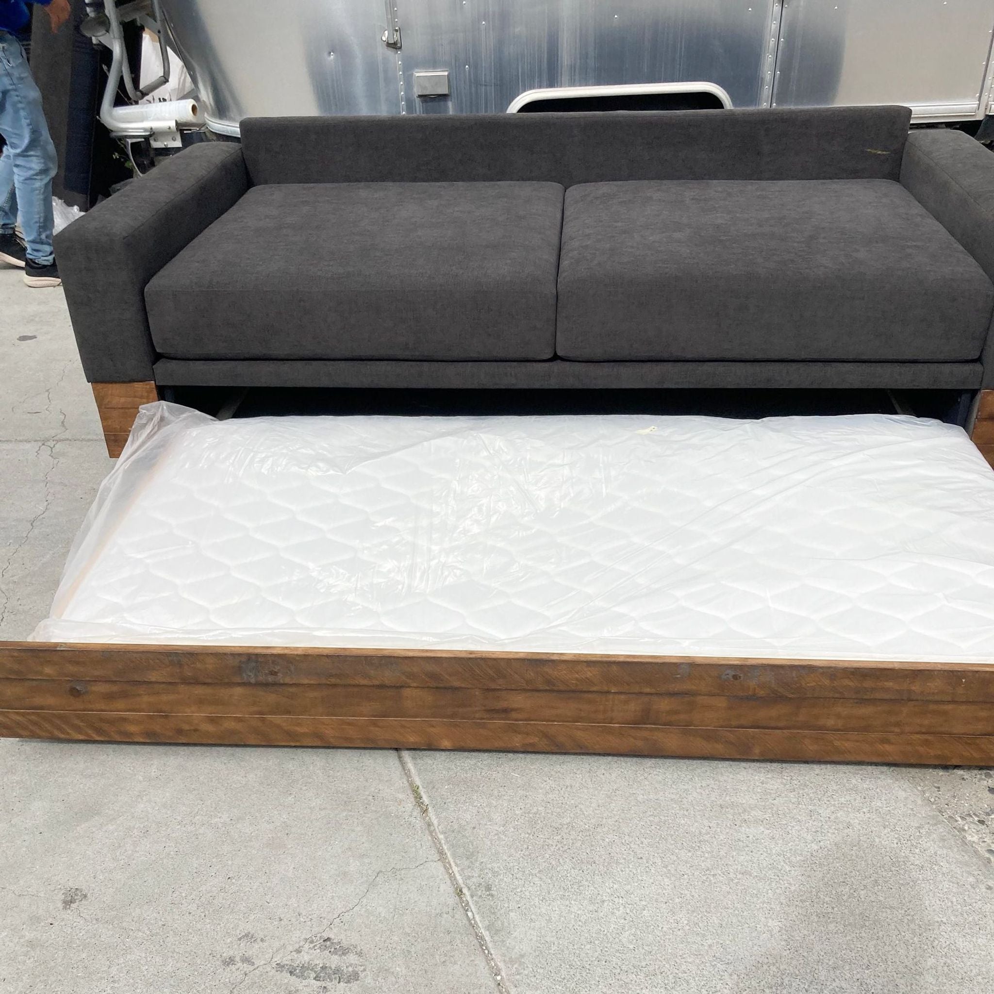 West Elm sleeper sofa with extended trundle on wheels, showcasing mattress and wooden base.