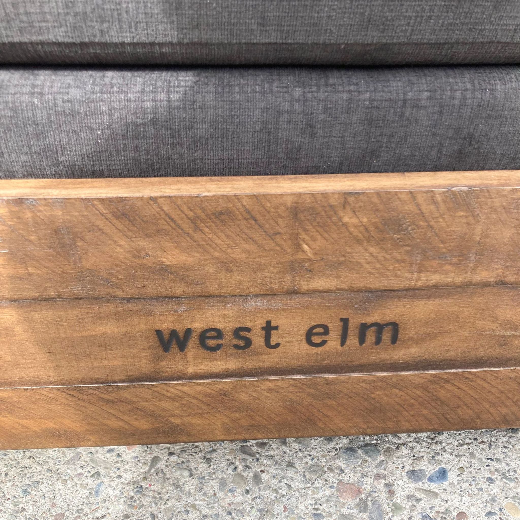 Close-up of West Elm branding on reclaimed wood base of charcoal sleeper sofa.