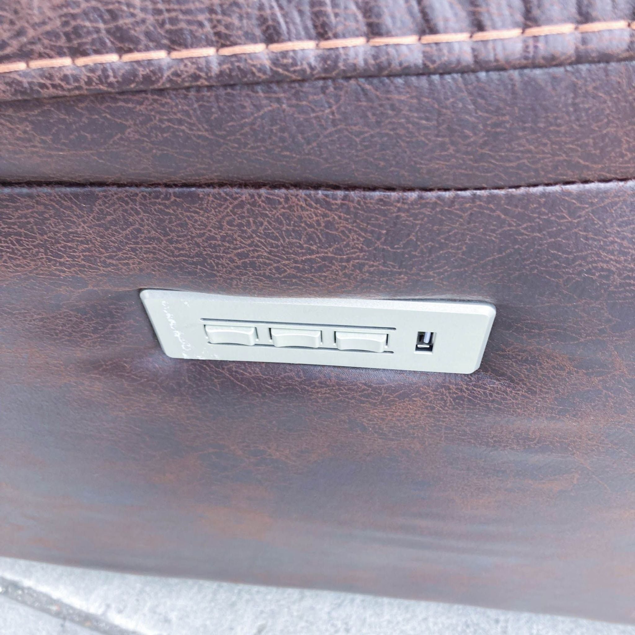 Close-up of built-in USB ports on the side of a brown faux leather loveseat for device charging.