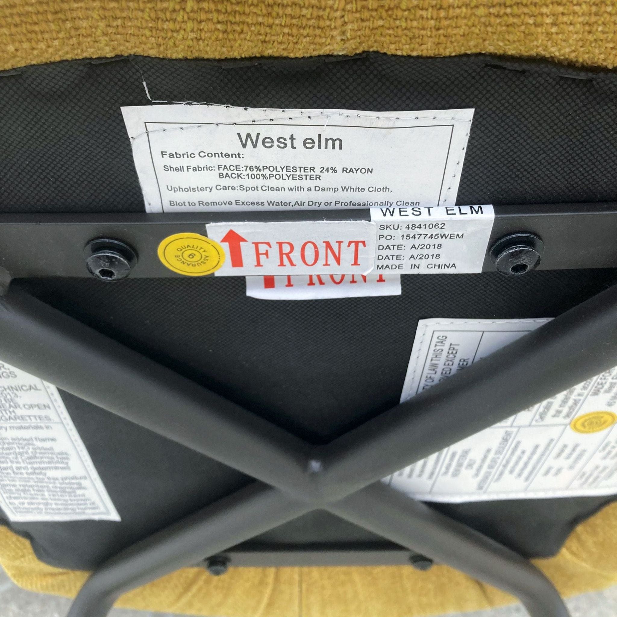 Underneath view of a West Elm dining chair showing fabric content label, quality control sticker, and care instructions.