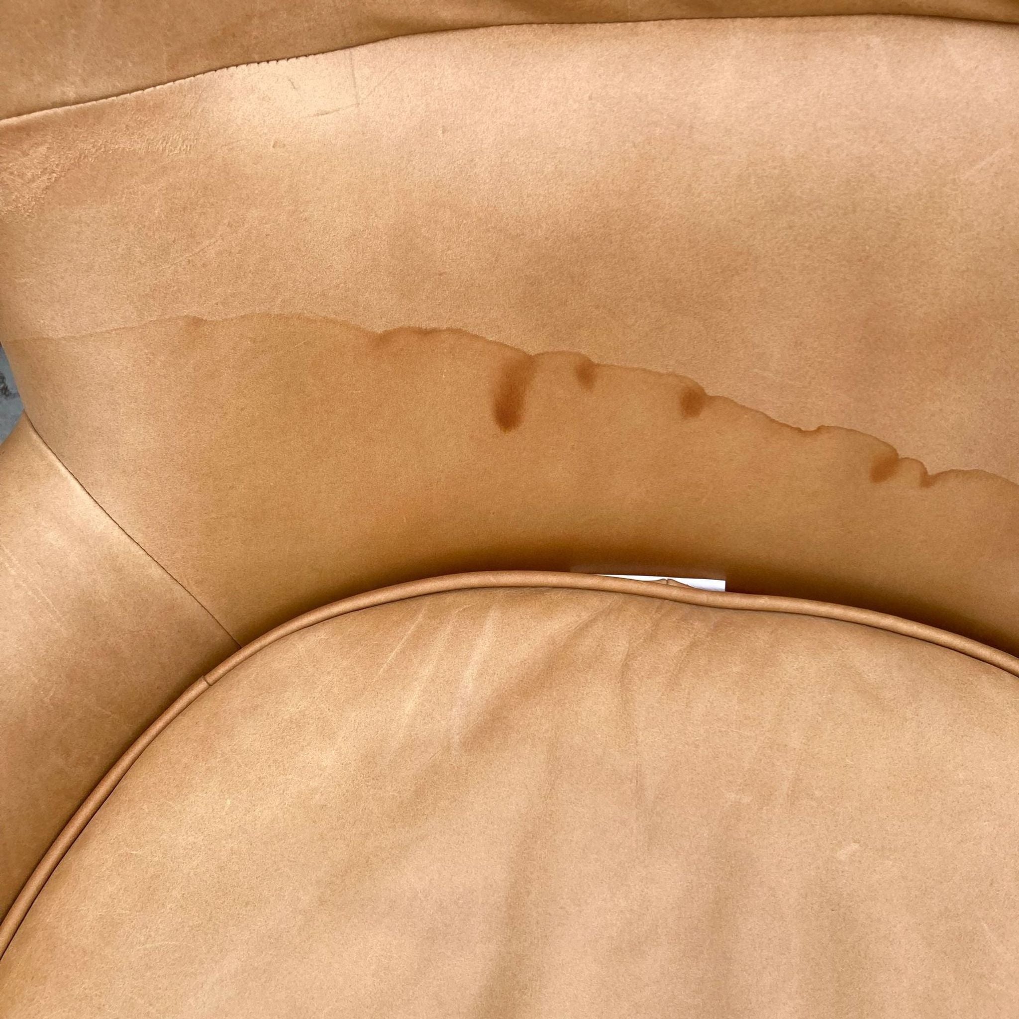Close-up of a tan leather chair cushion with water stains and a visible pen between creases.