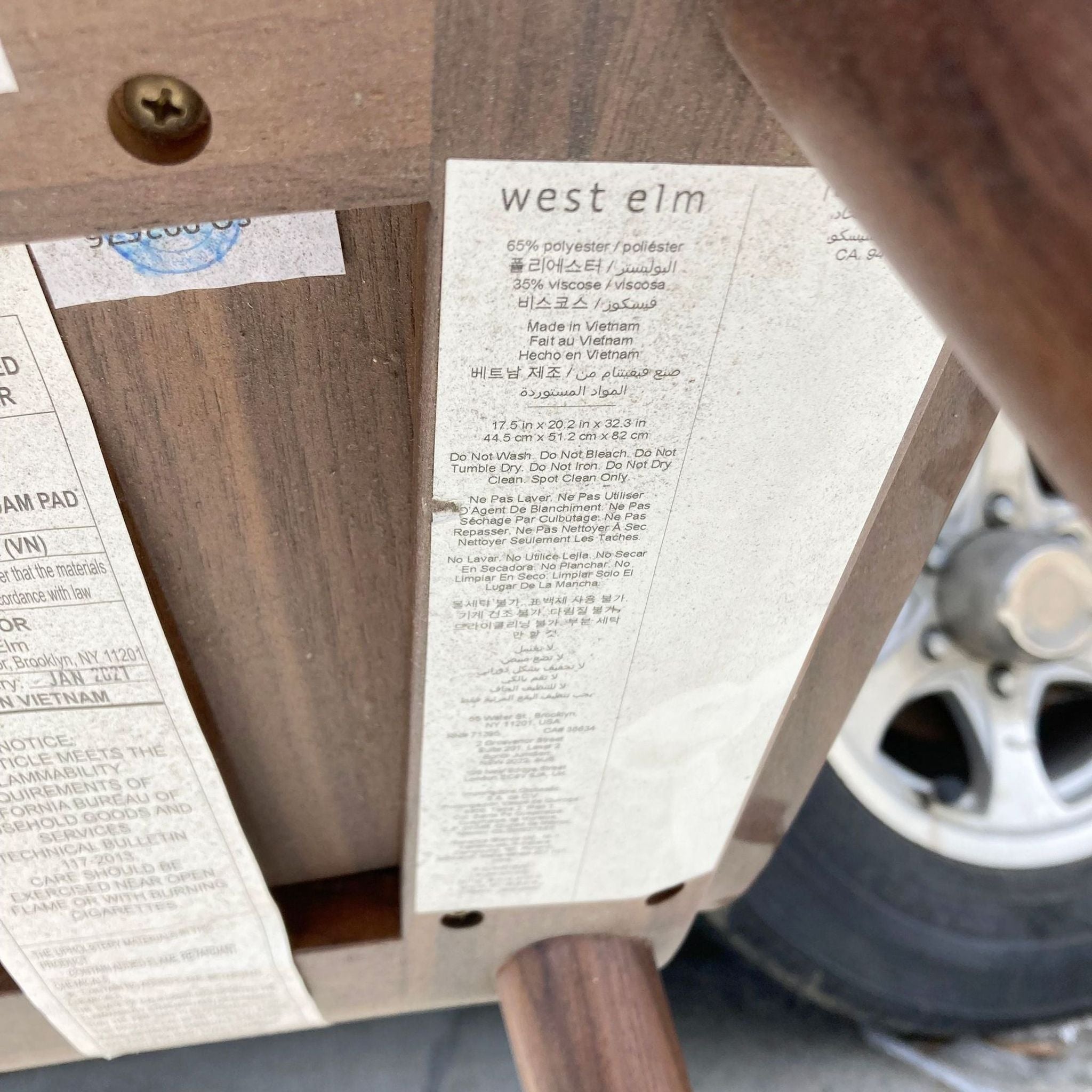 2. Close-up of a West Elm label on the underside of a wooden chair, detailing materials and care instructions.