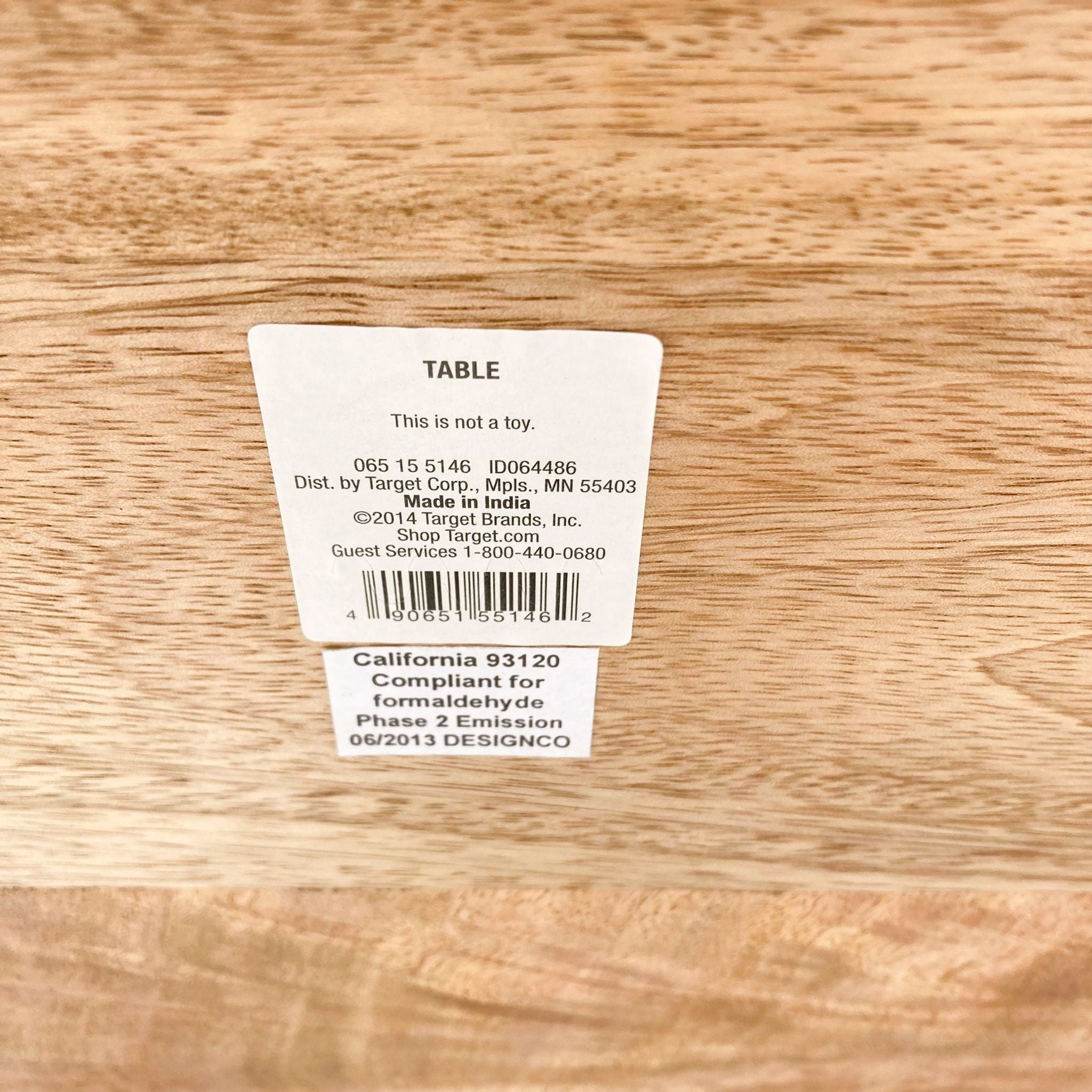 Label on wood surface indicating a Target brand table, not a toy, with compliance and contact information.