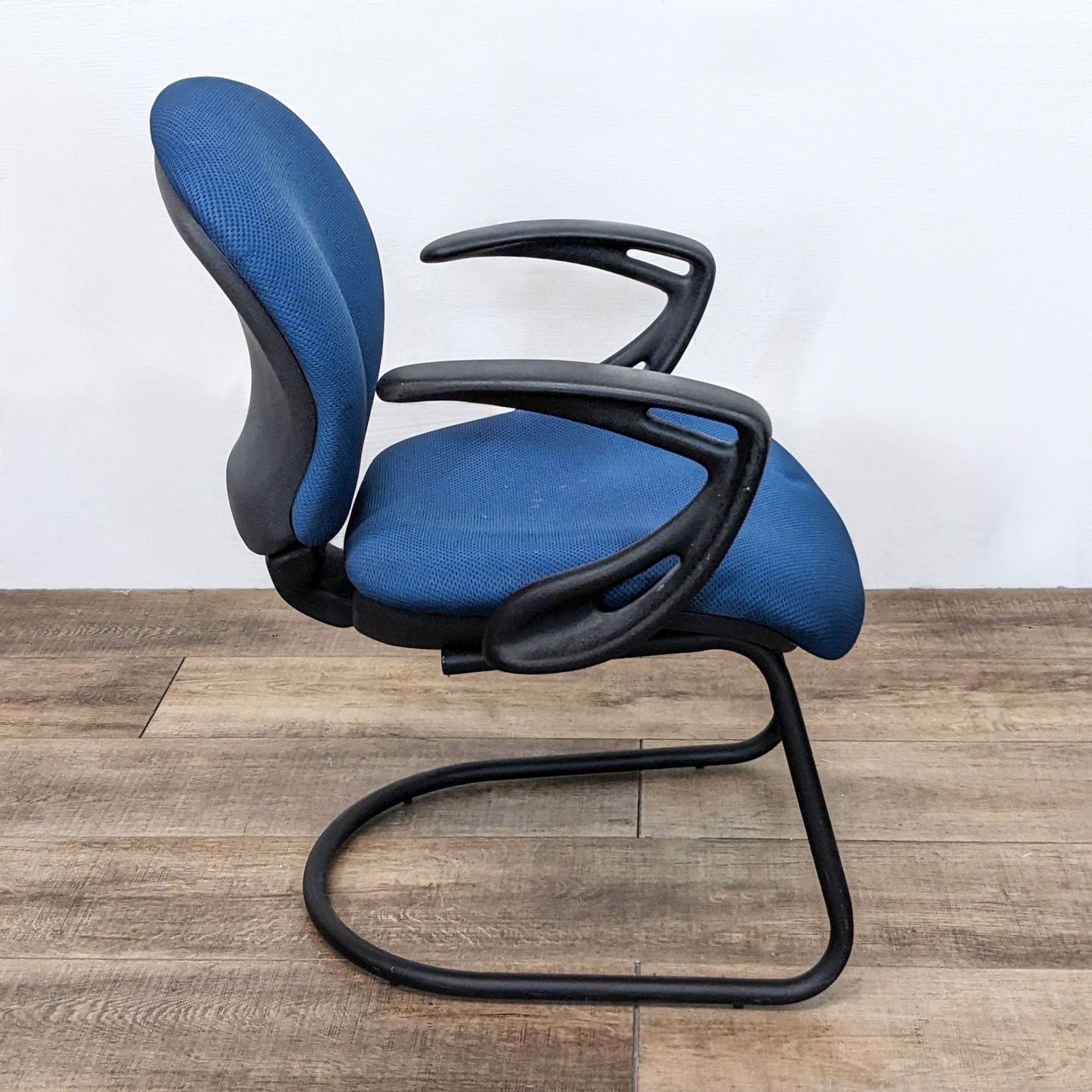 3. "Angle view showcasing the side and curved armrests of a blue Reperch office chair on a wooden floor."