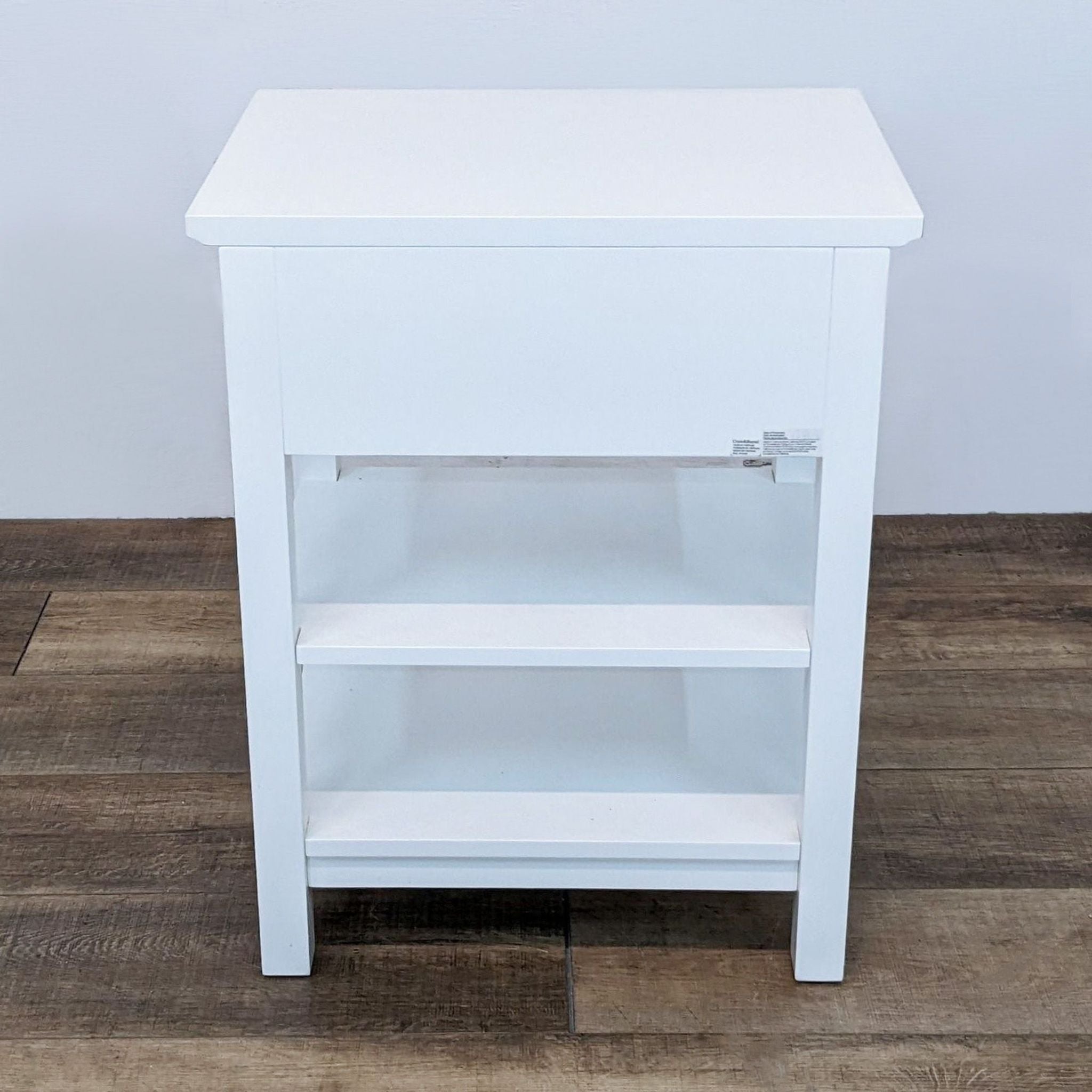 3. Front view of a white Crate & Barrel end table with a closed drawer and an open lower shelf, against a plain background.