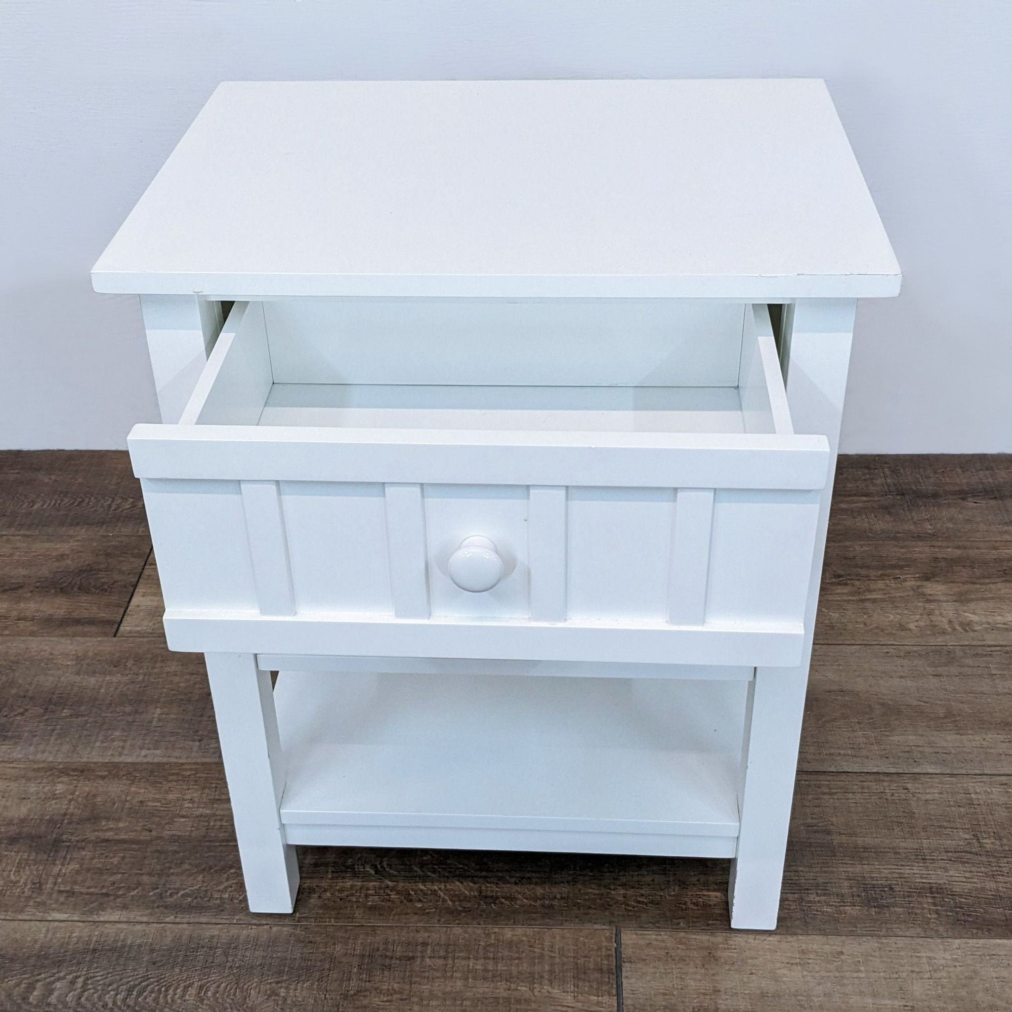 2. A white Crate & Barrel end table, drawer slightly open, revealing storage space, on hardwood flooring.