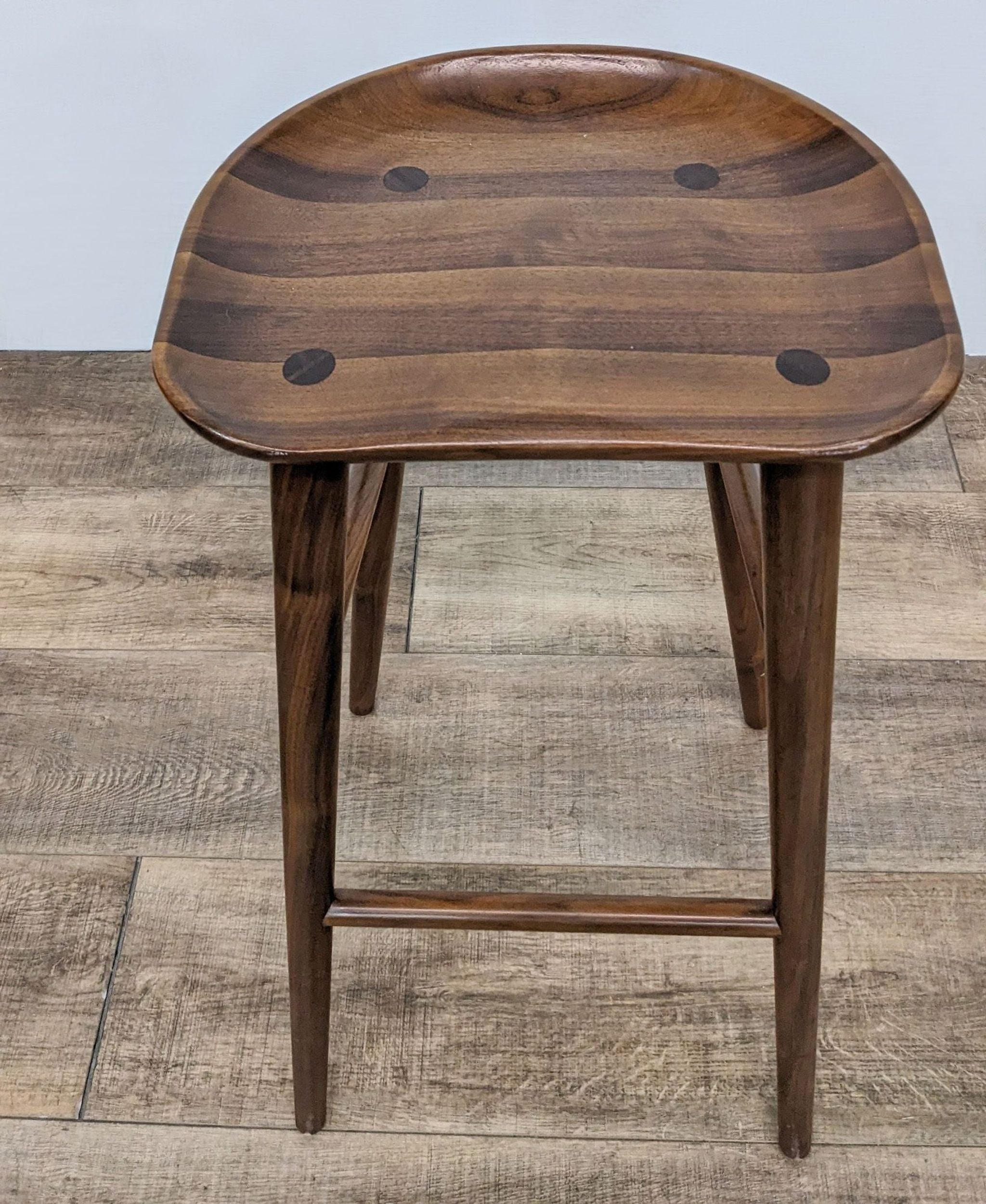 2. Top-down view of a dark wooden stool showing stripes and circular marks on the seat, with robust legs on a textured floor.