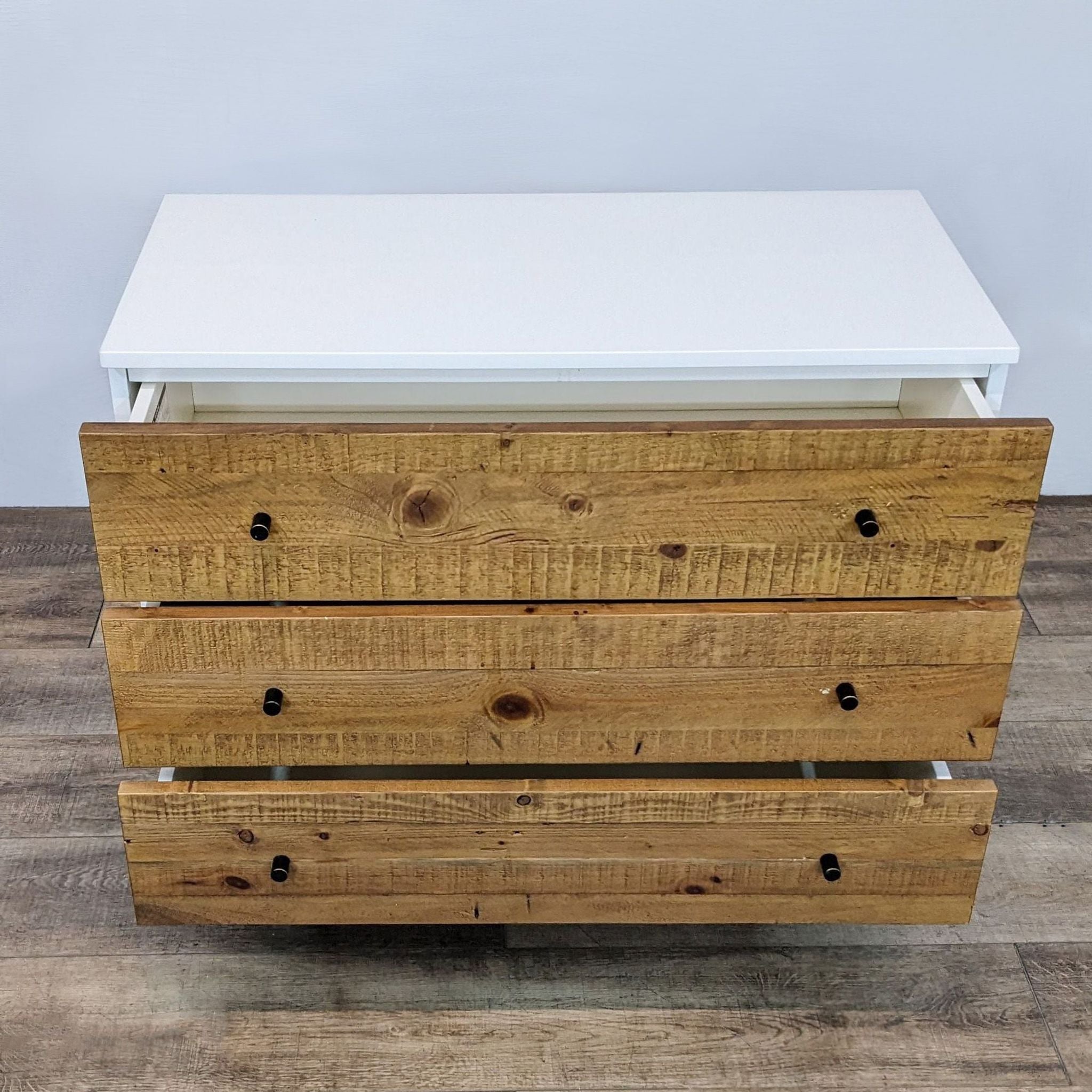 2. Opened reclaimed wood-style drawers of a West Elm dresser with white casing on a wood floor.