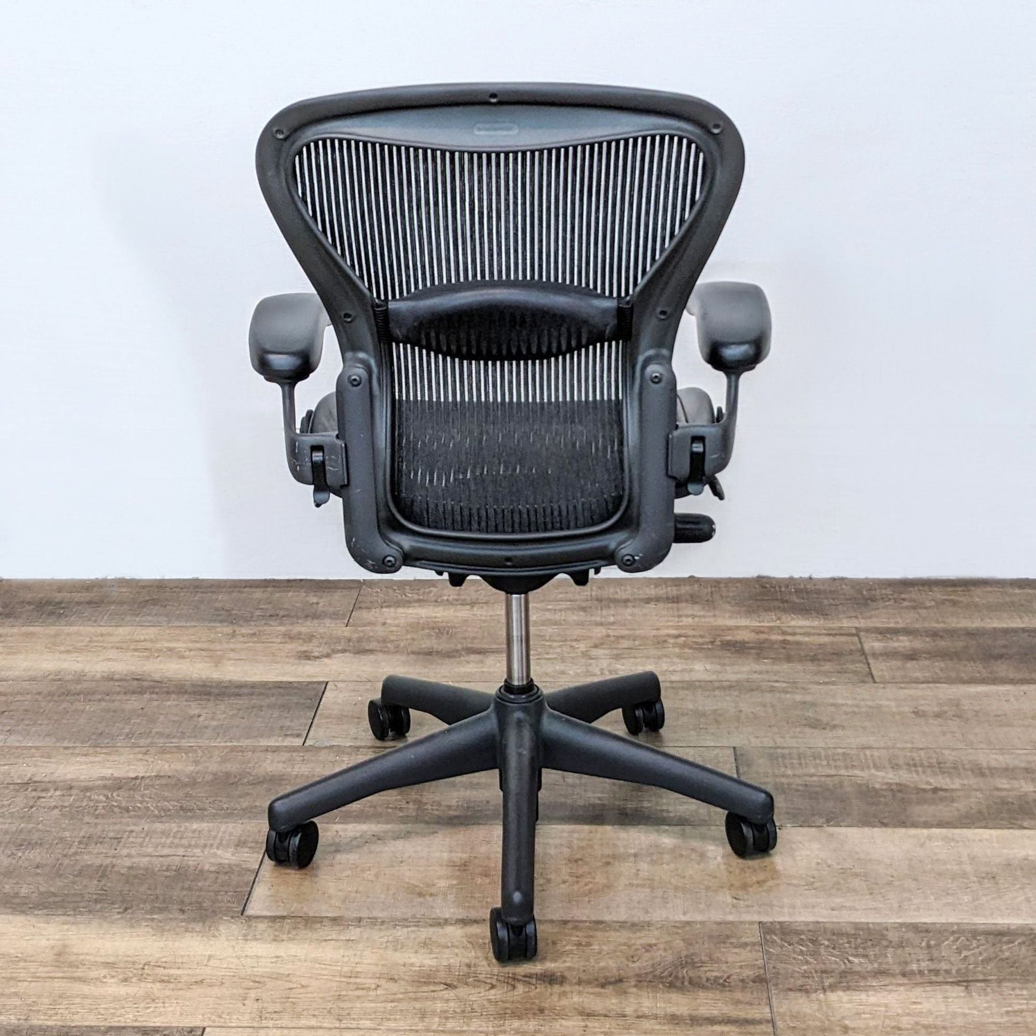 Medium-sized Aeron office chair by Herman Miller, featuring lumbar support, on a wooden floor with adjustable features.