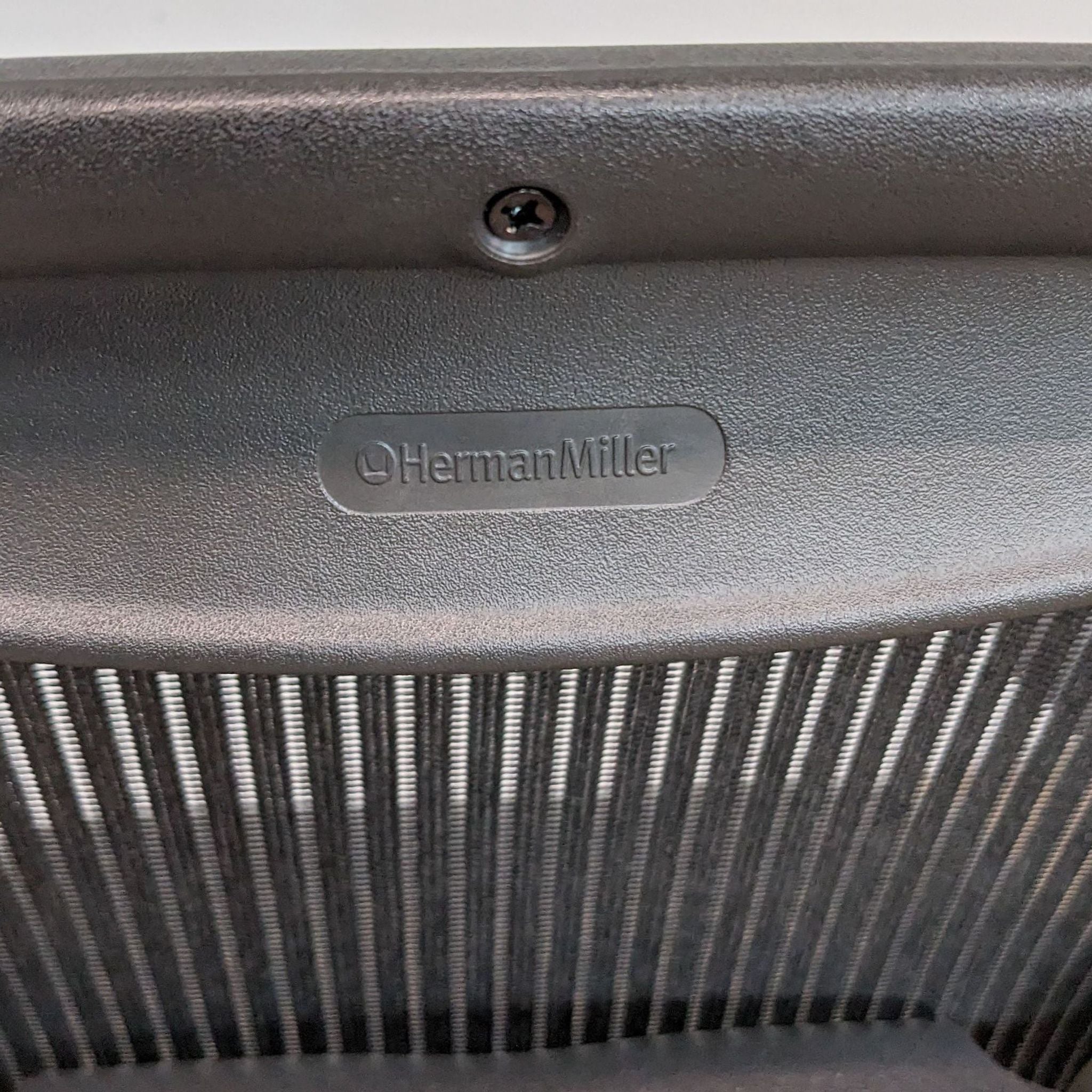 Close-up of a Herman Miller logo on an Aeron chair with black mesh, symbolizing quality ergonomic office furniture.