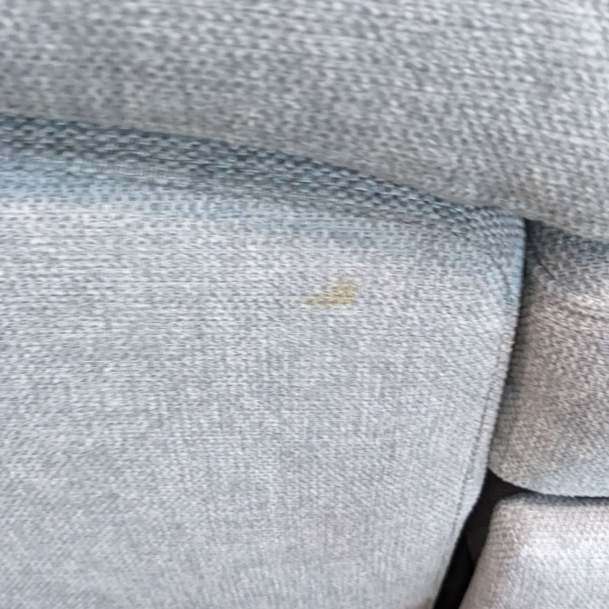 3. Close-up of a light stain on the gray fabric of a Reperch modular sectional, detailing the texture and quality of the material.