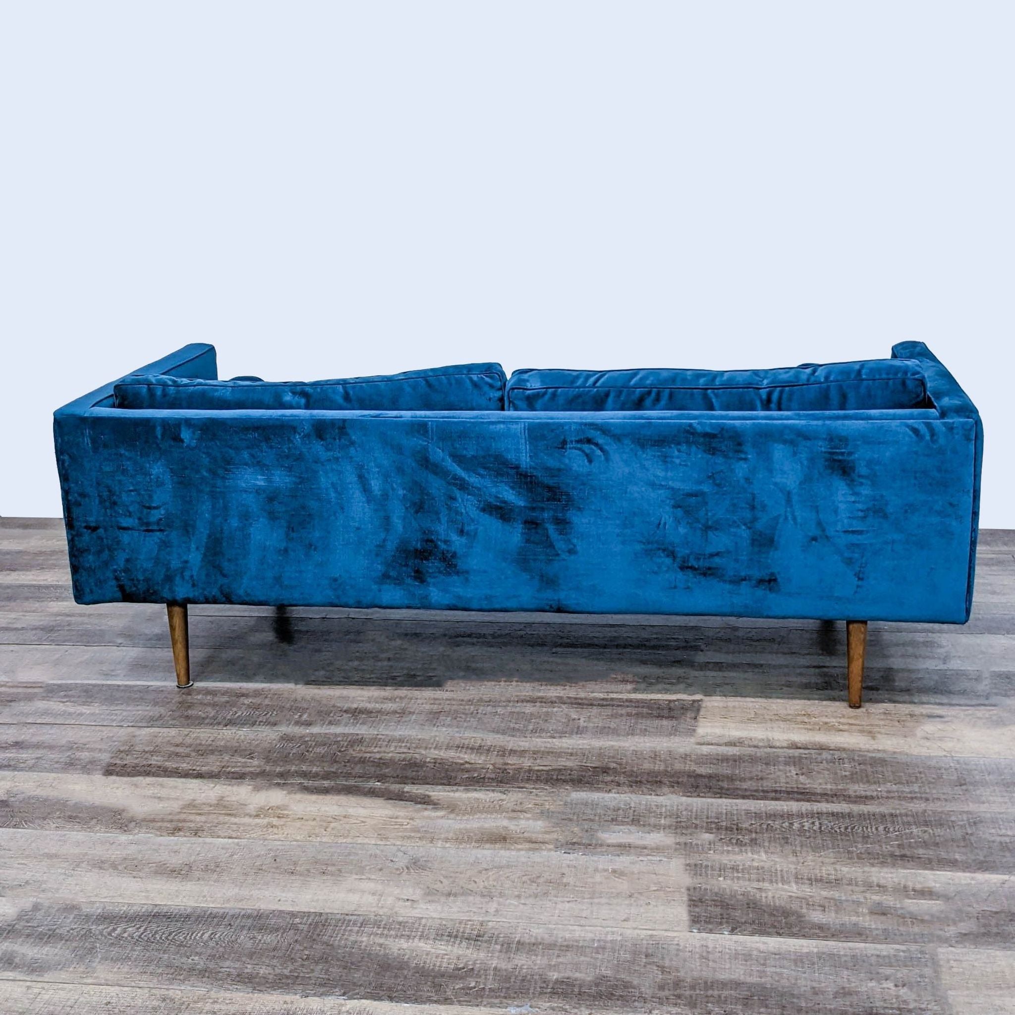 3. Side view showing the sleek design of a West Elm 3-seat blue velvet couch with tapered wooden legs.