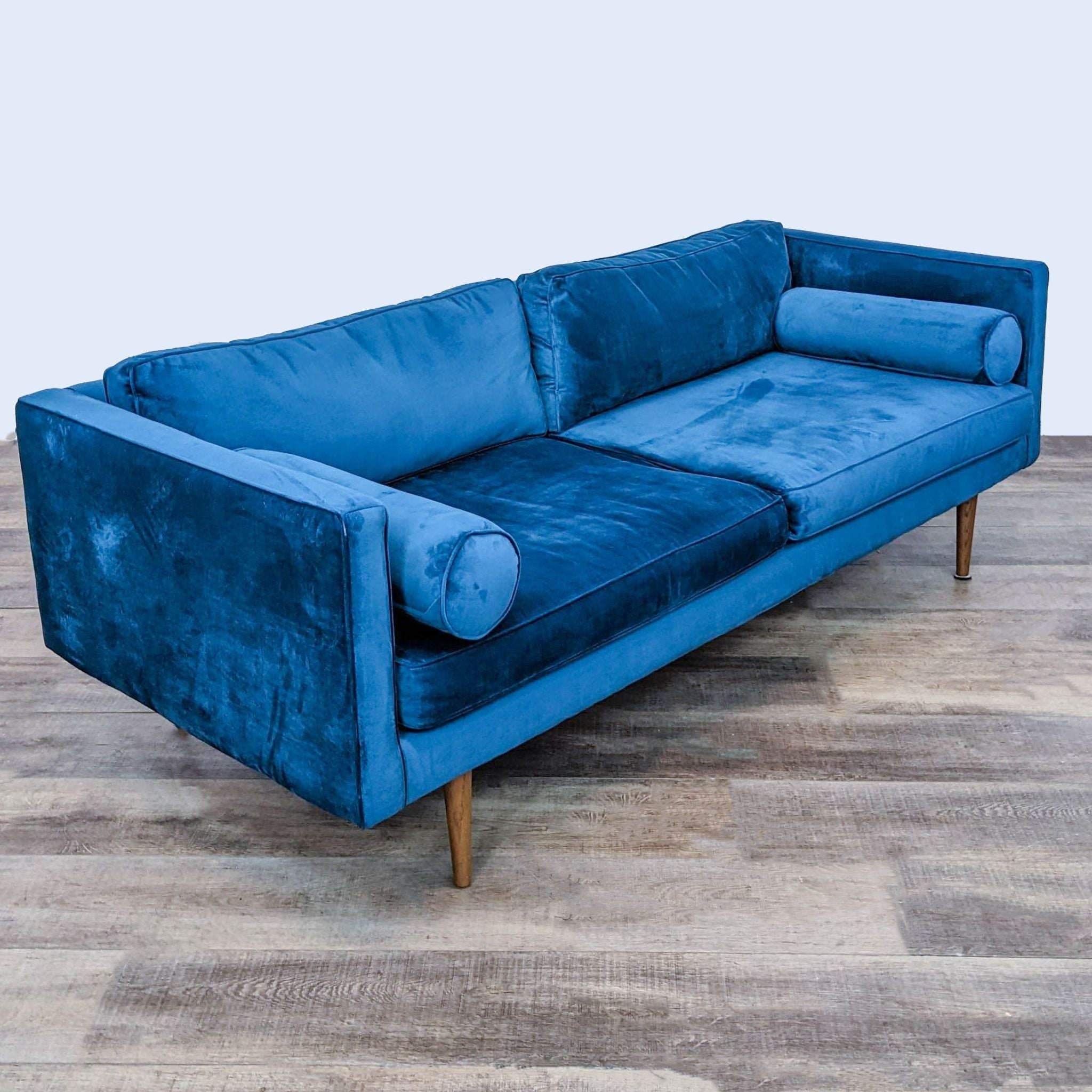 2. Front angled view of a glamorous West Elm blue velvet sofa with clean modern styling and bolster pillows.