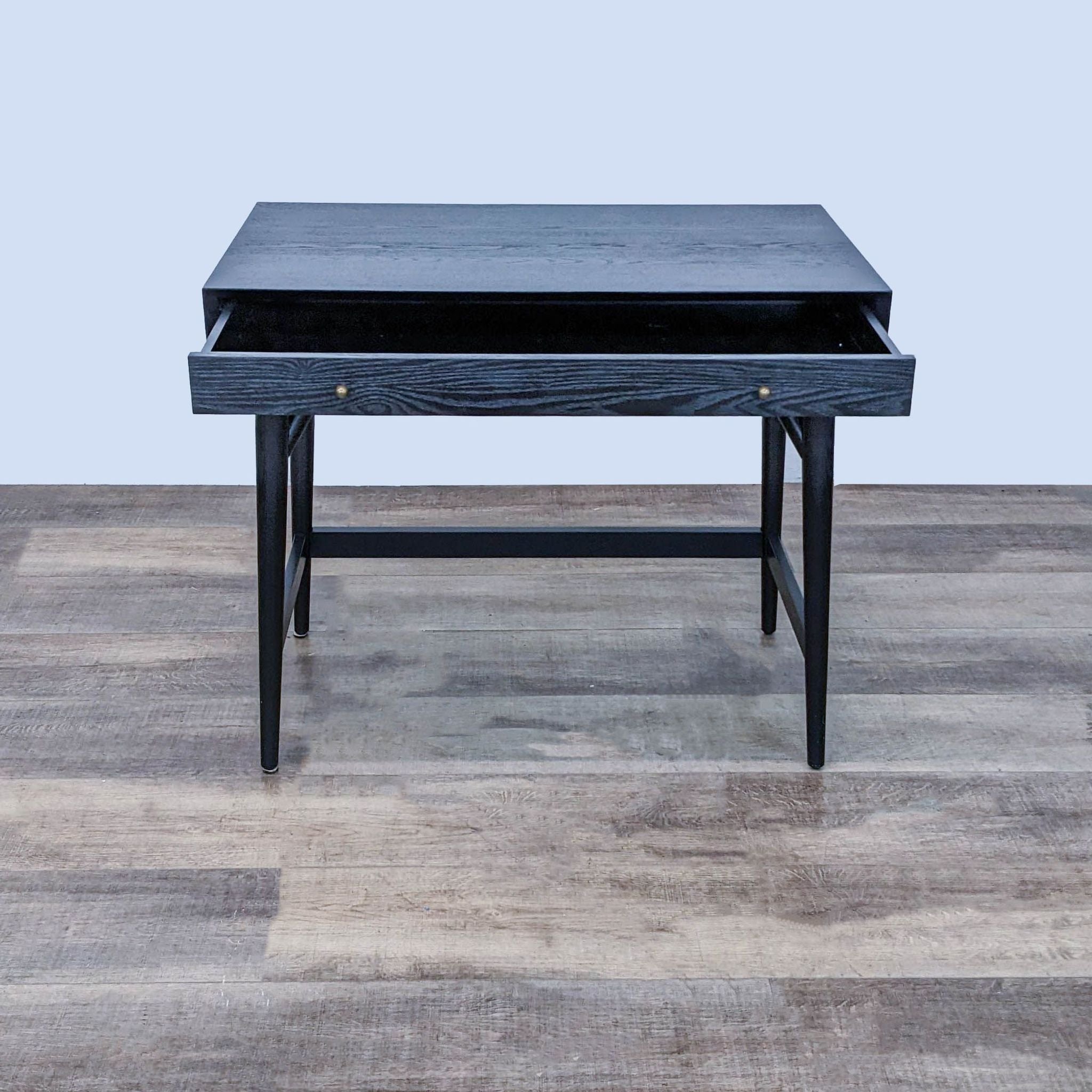 West Elm black writing desk with drawer open to show storage, metal handles, standing on a wooden floor.