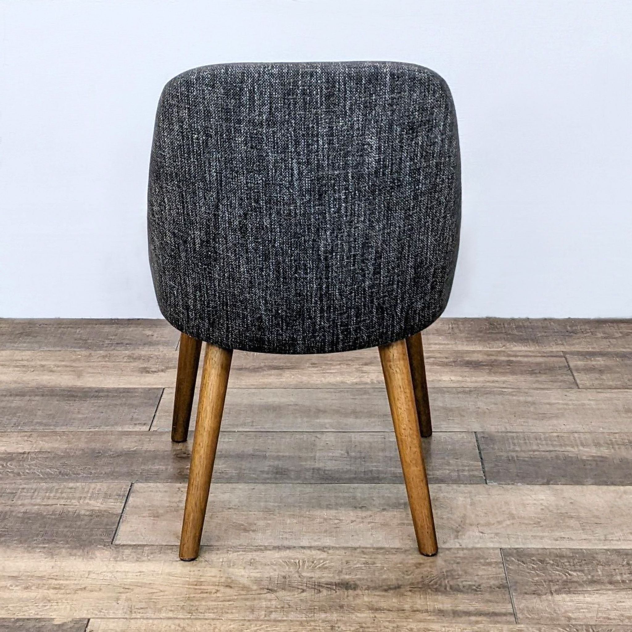 Rear view of a West Elm Mid-Century Dining Chair, emphasizing the chair's sloping back and tapered wooden legs on a wooden floor.