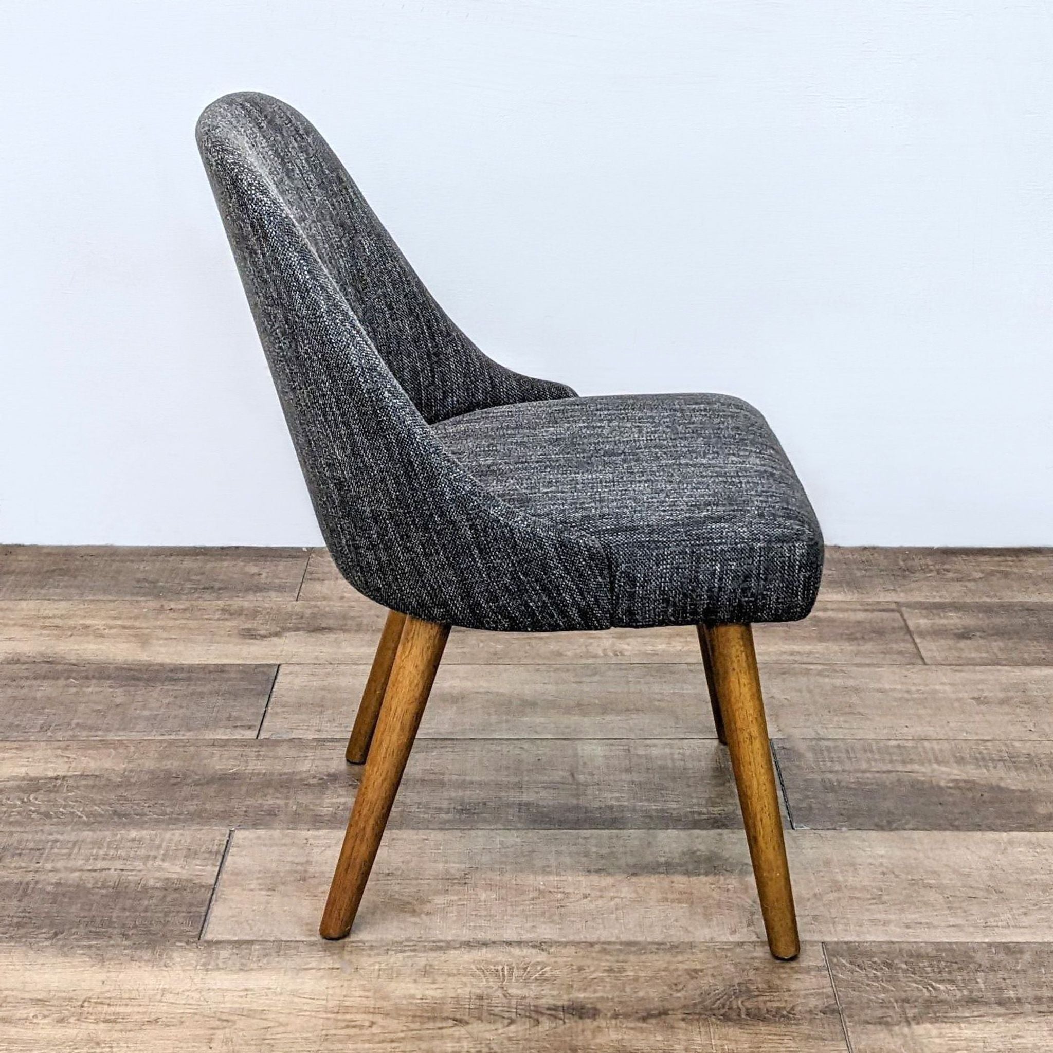 Side view of West Elm Mid-Century Dining Chair, showcasing the sloping back and retro-inspired wide seat against a wooden floor.