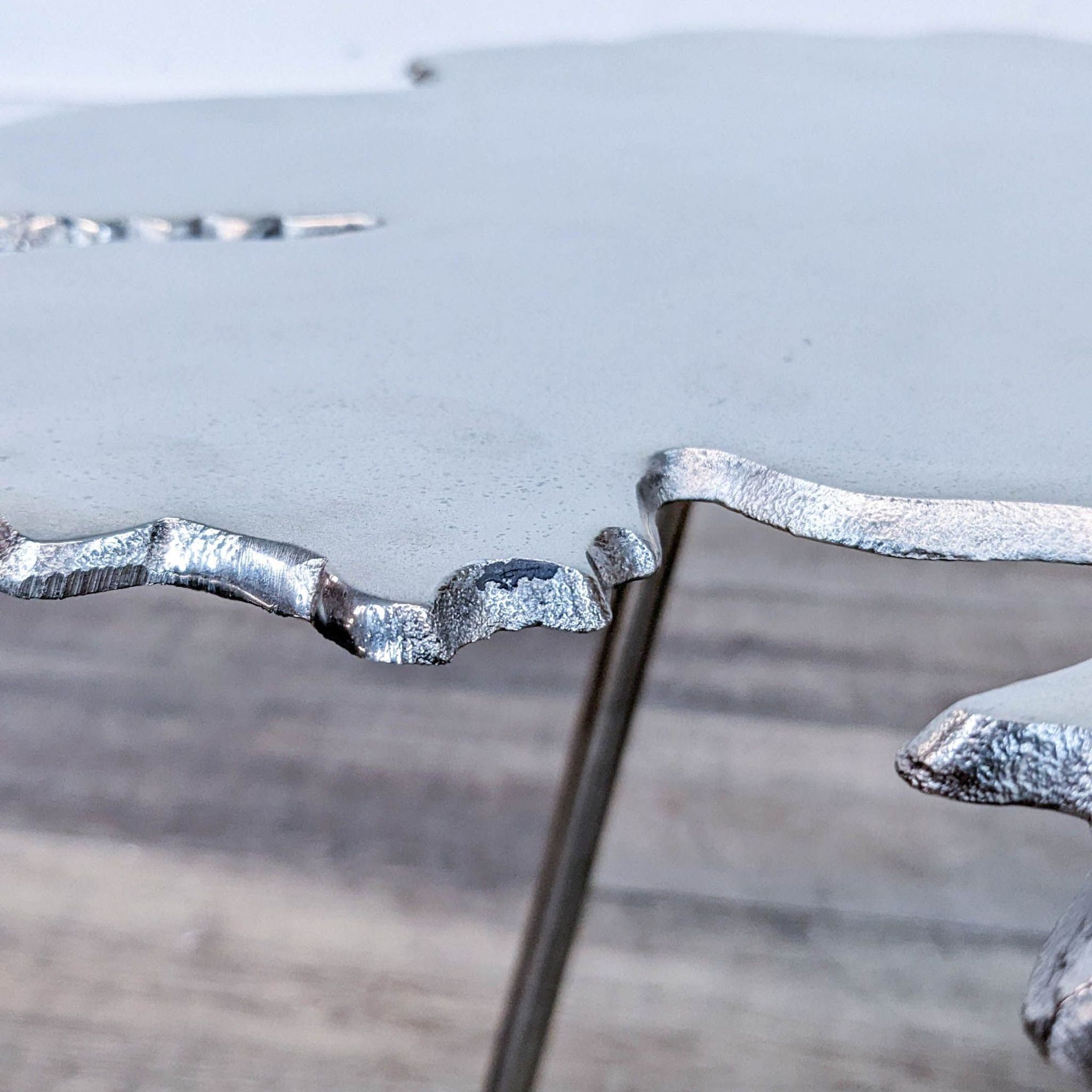 Detail of the Reperch end table's edge, showing the textured, irregular border and one of the supporting metal legs.