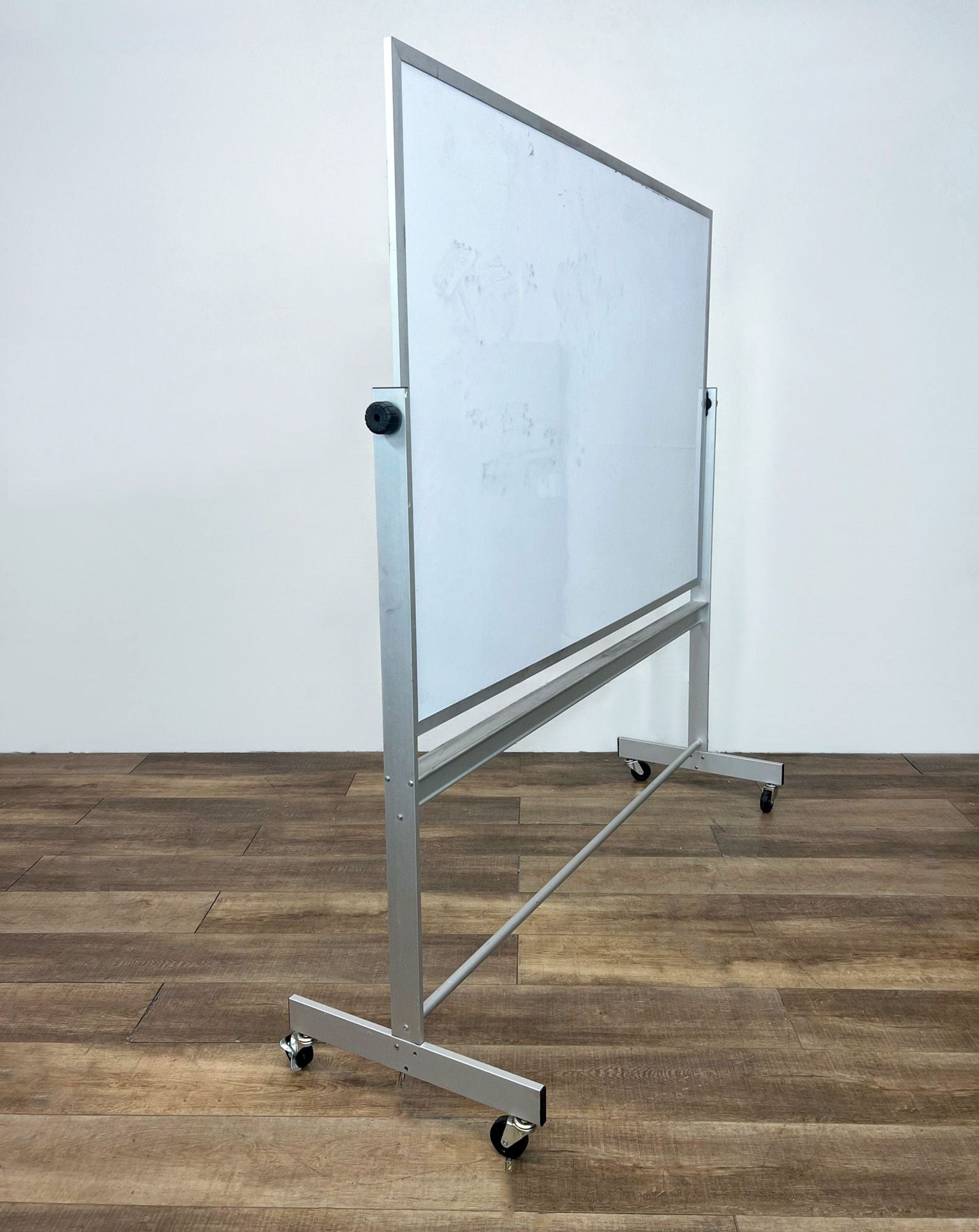 A side view of a Reperch magnetic whiteboard with a steel frame and casters on a wooden floor.