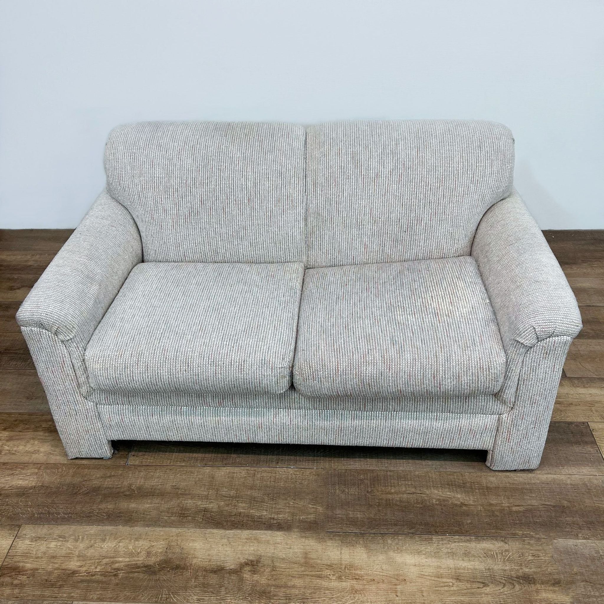 2. Front view of a Reperch tweed pattern fabric loveseat with cushioned backs and arms on a wooden floor.