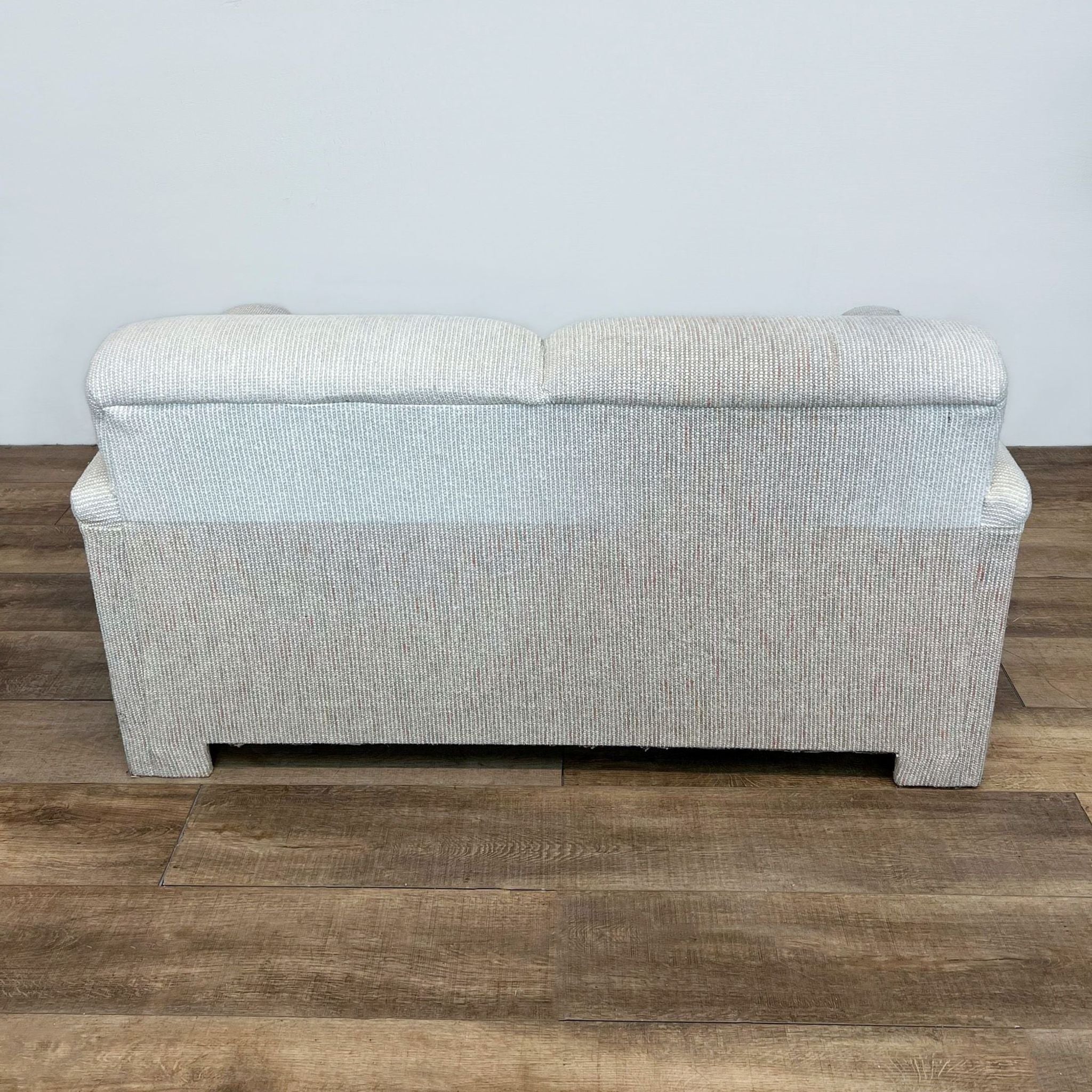 3. Rear perspective of a tweed upholstered Reperch loveseat with a straight back design, standing on a laminate floor.