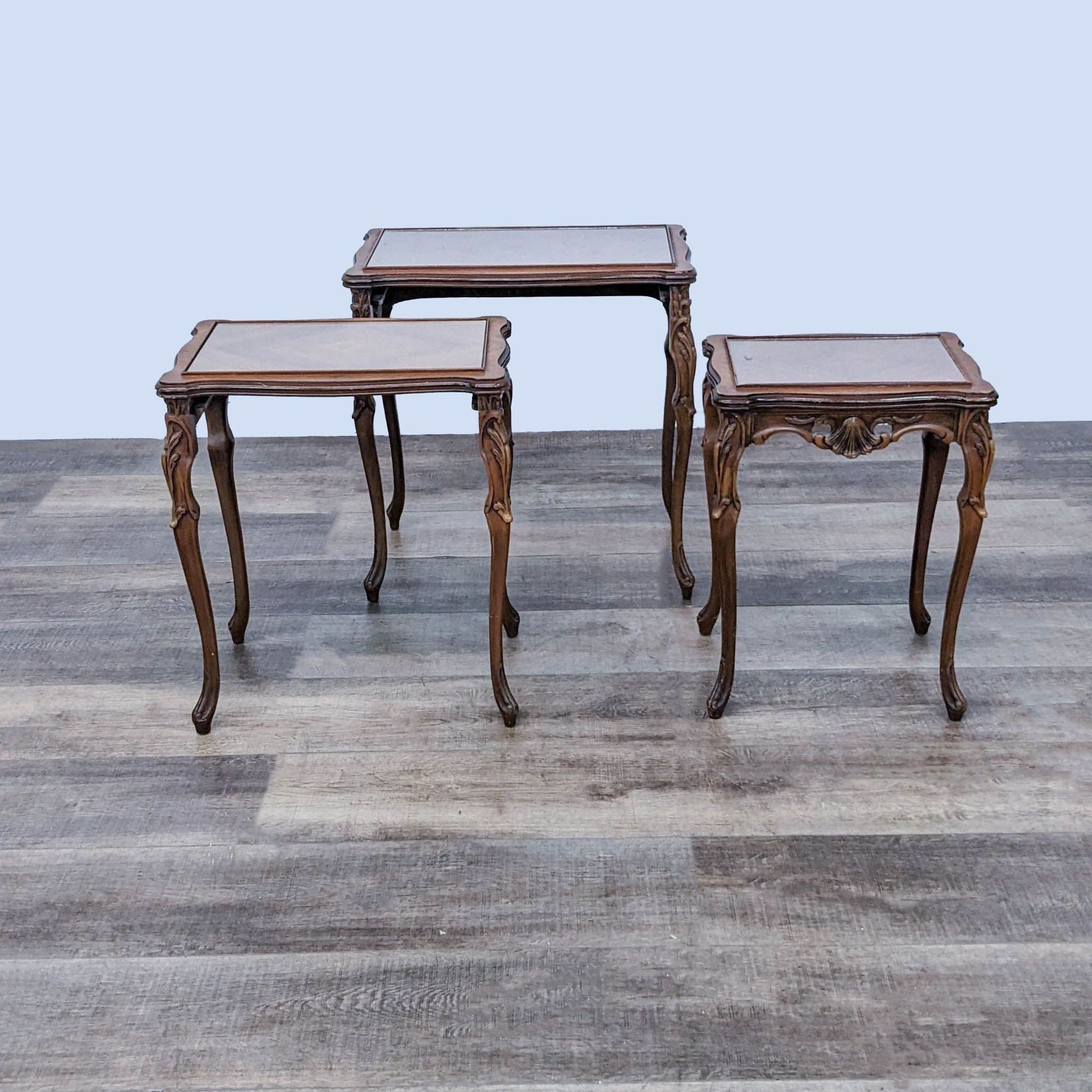 Trio of carved Reperch end tables featuring glass tops and curved legs, on a patterned floor.