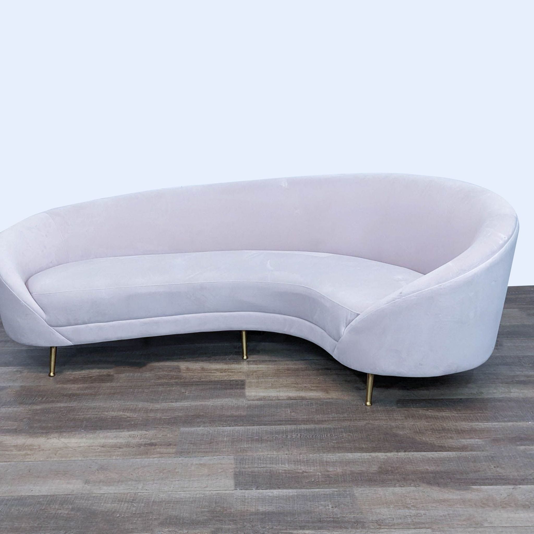 2. Hollywood Vibe curved white sofa designed for three people, featuring a sleek design and gold feet against a wood-patterned background.